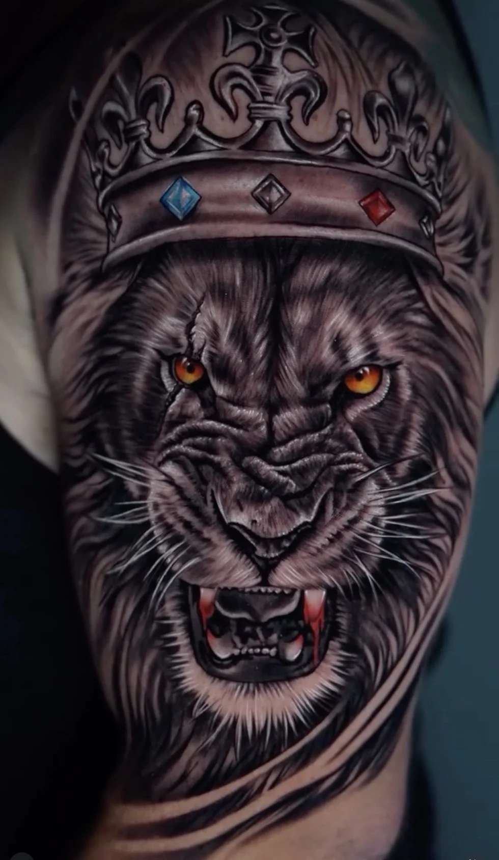 A detailed tattoo of a fierce lion with a crown on its head, showing bared fangs and intense orange eyes.
