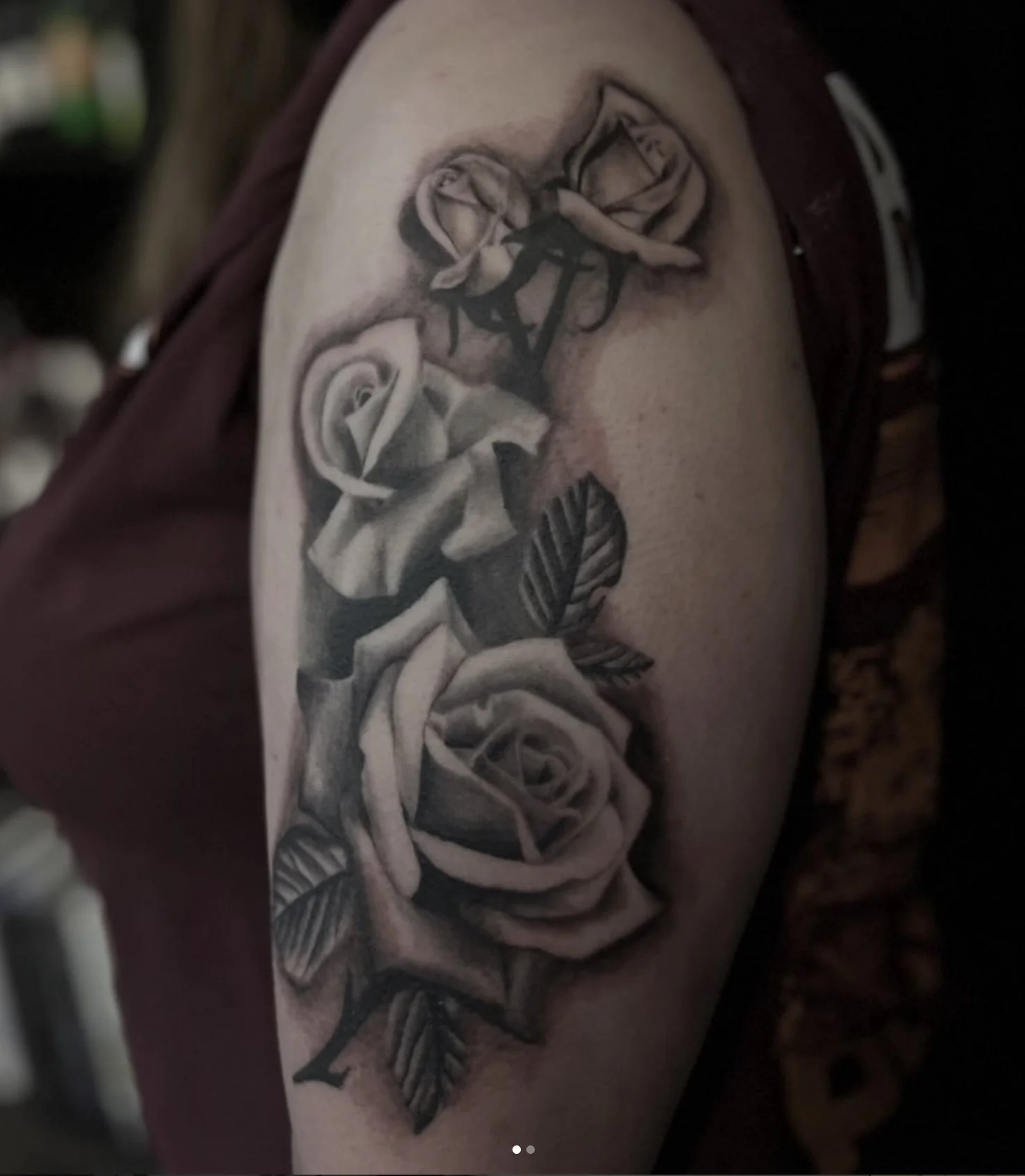 A tattoo of a realistic rose with leaves on a person's upper arm.