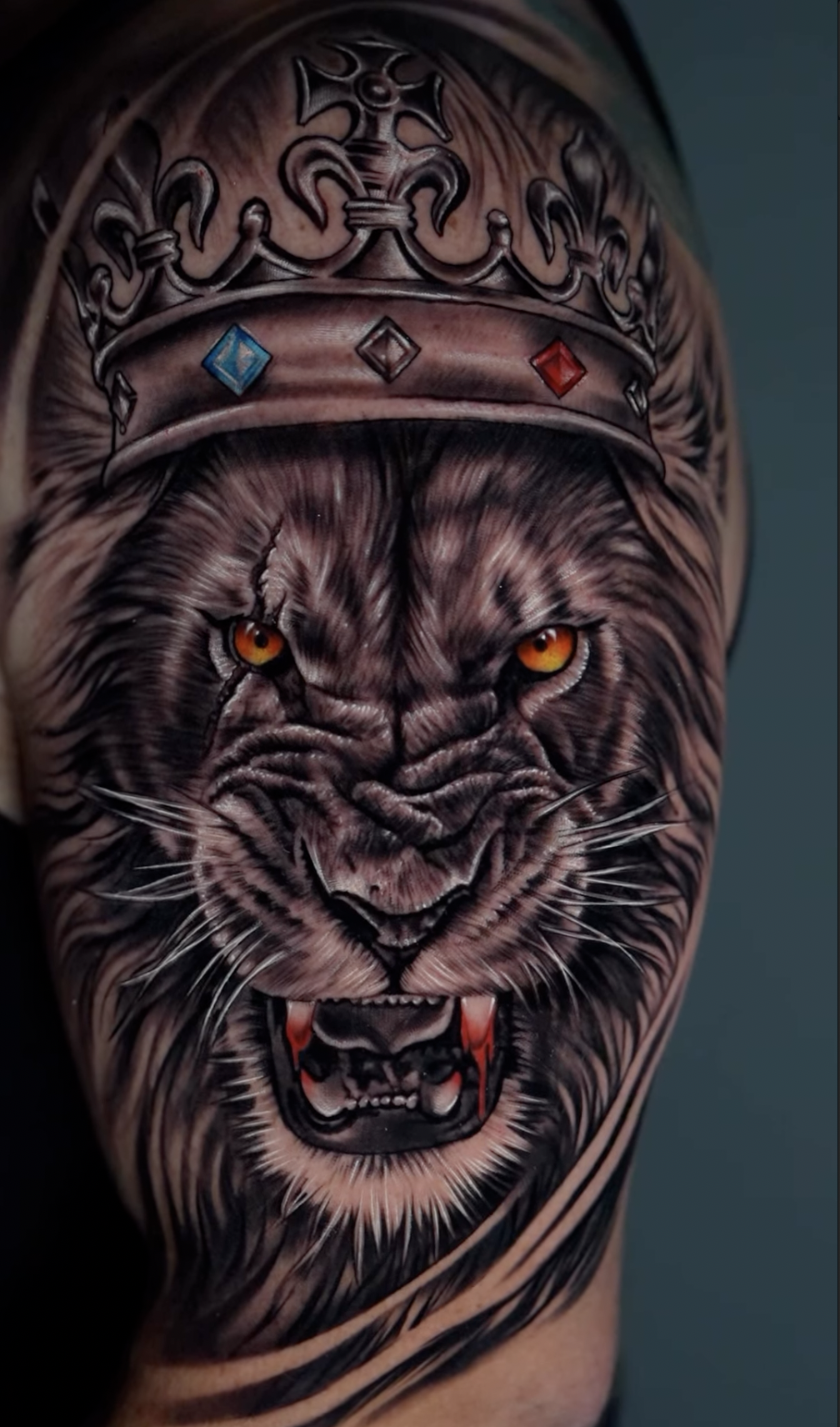 Tattoo of a fierce tiger with orange eyes, wearing a crown with blue, black, and red jewels.