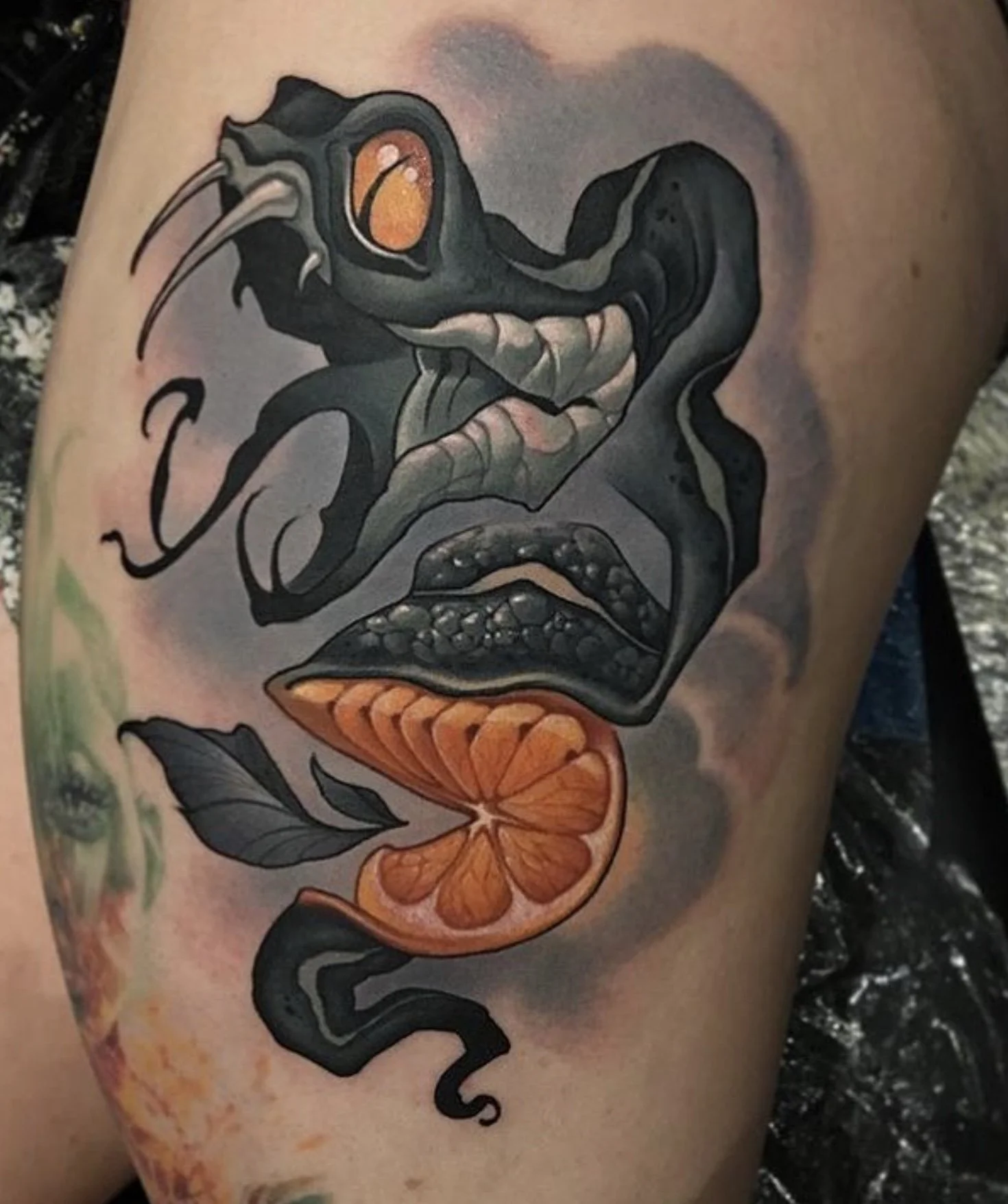 Tattoo of a snake intertwined with a human face and an orange slice.