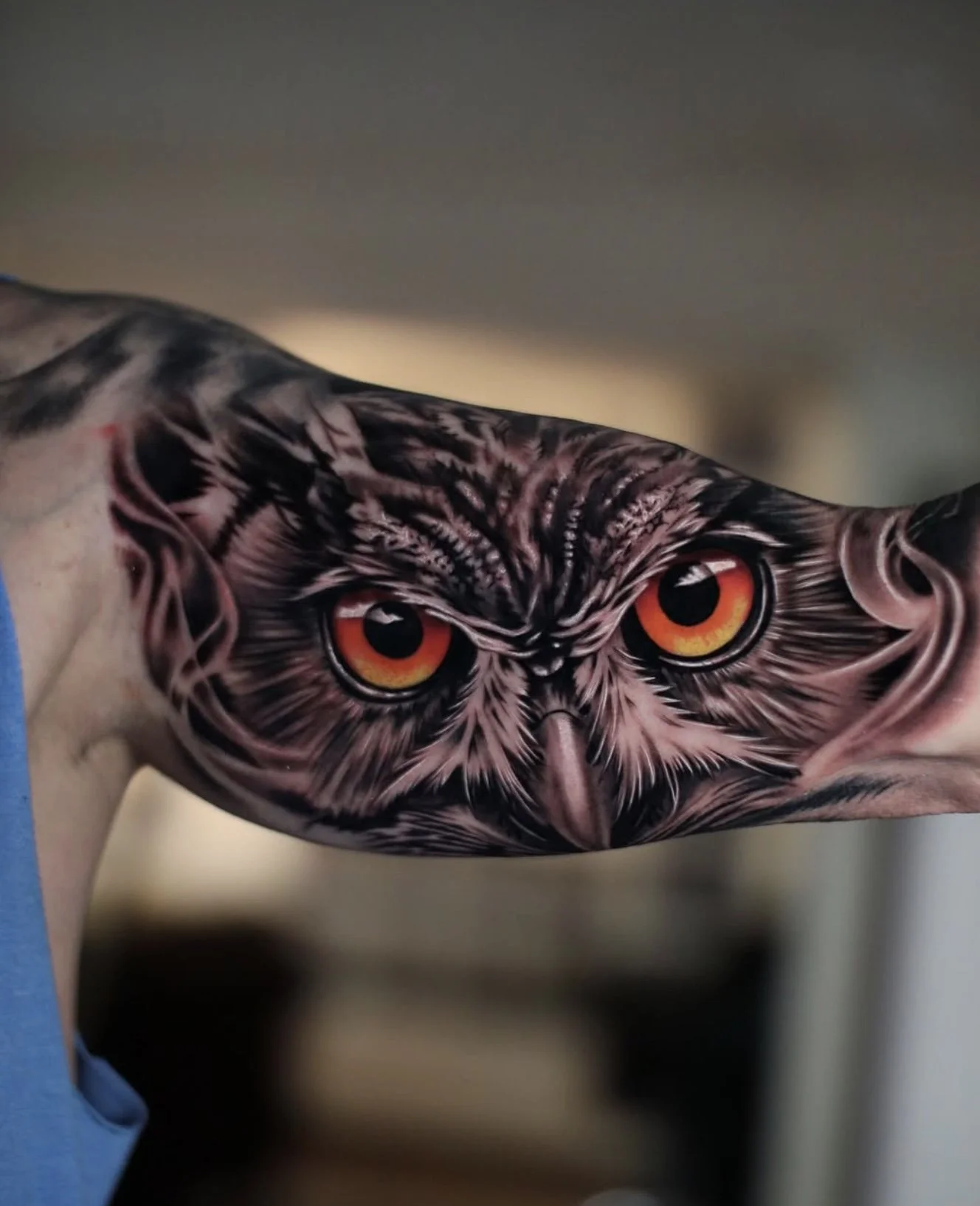 Tattoo of an owl with orange eyes on a person's upper arm.