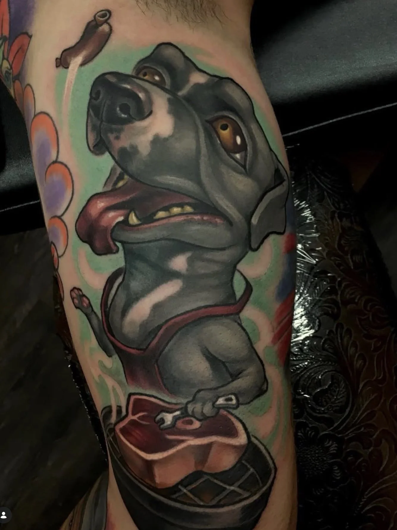 Colorful tattoo on person's arm depicting a dog's face with a serious expression, tongue sticking out, and a collar, with abstract designs and vivid colors.