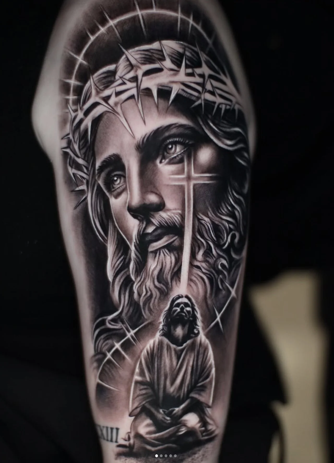 Black and gray tattoo of Jesus Christ with a halo and crown of thorns, featuring a cross on his face, and a praying figure at the bottom.