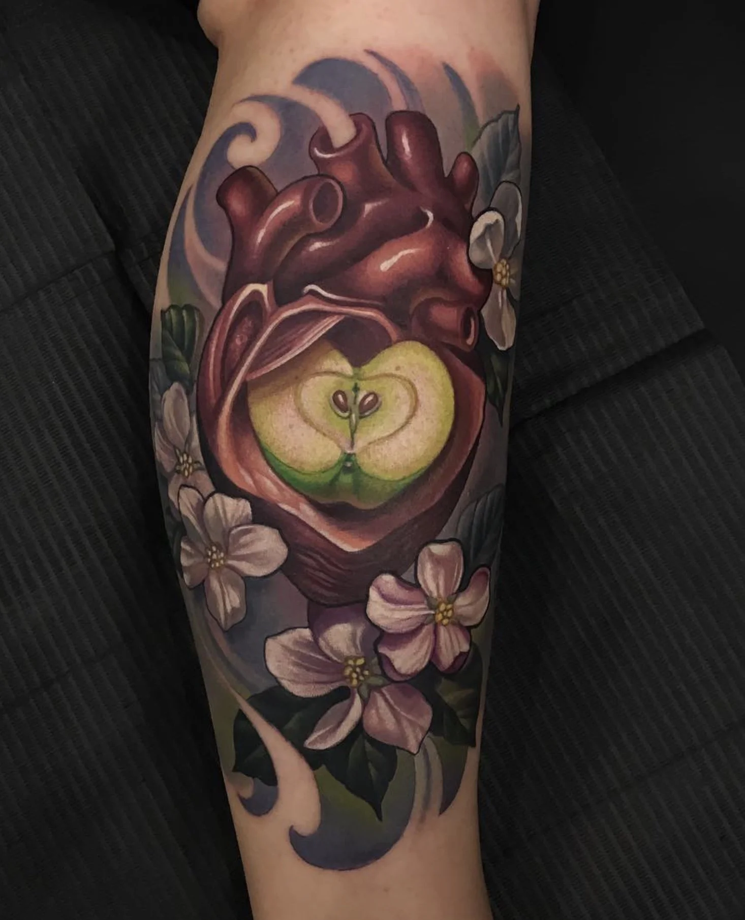 Tattoo of a realistic human heart with a sliced apple inside it, surrounded by cherry blossoms.