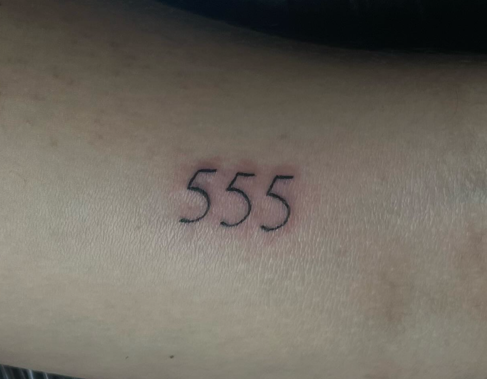 Close-up of a small tattoo of the number '555' on light skin.