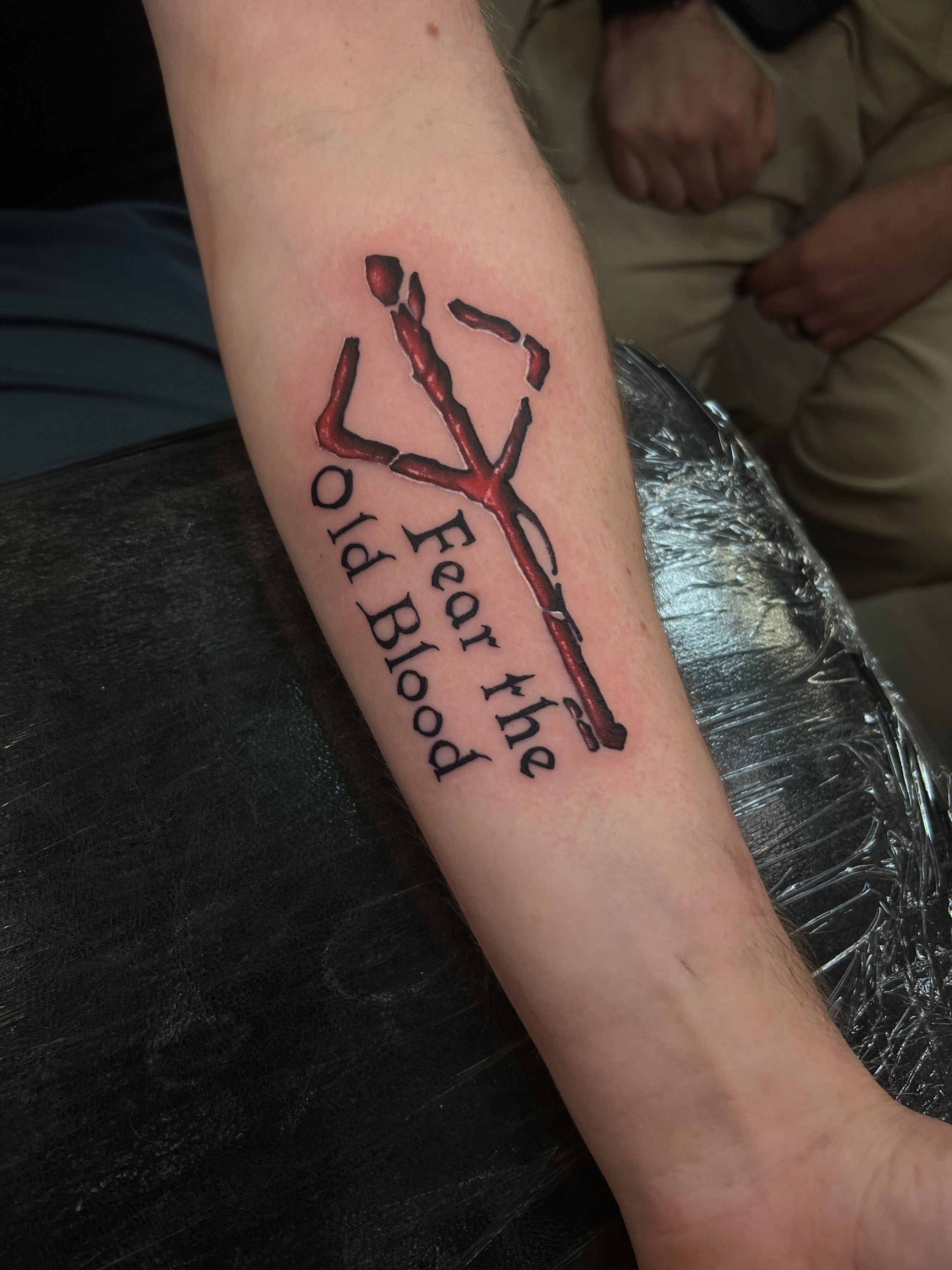 Tattoo on person's forearm showing a bloodstained axe and the words 'Eat the Pody Blood' beneath it.