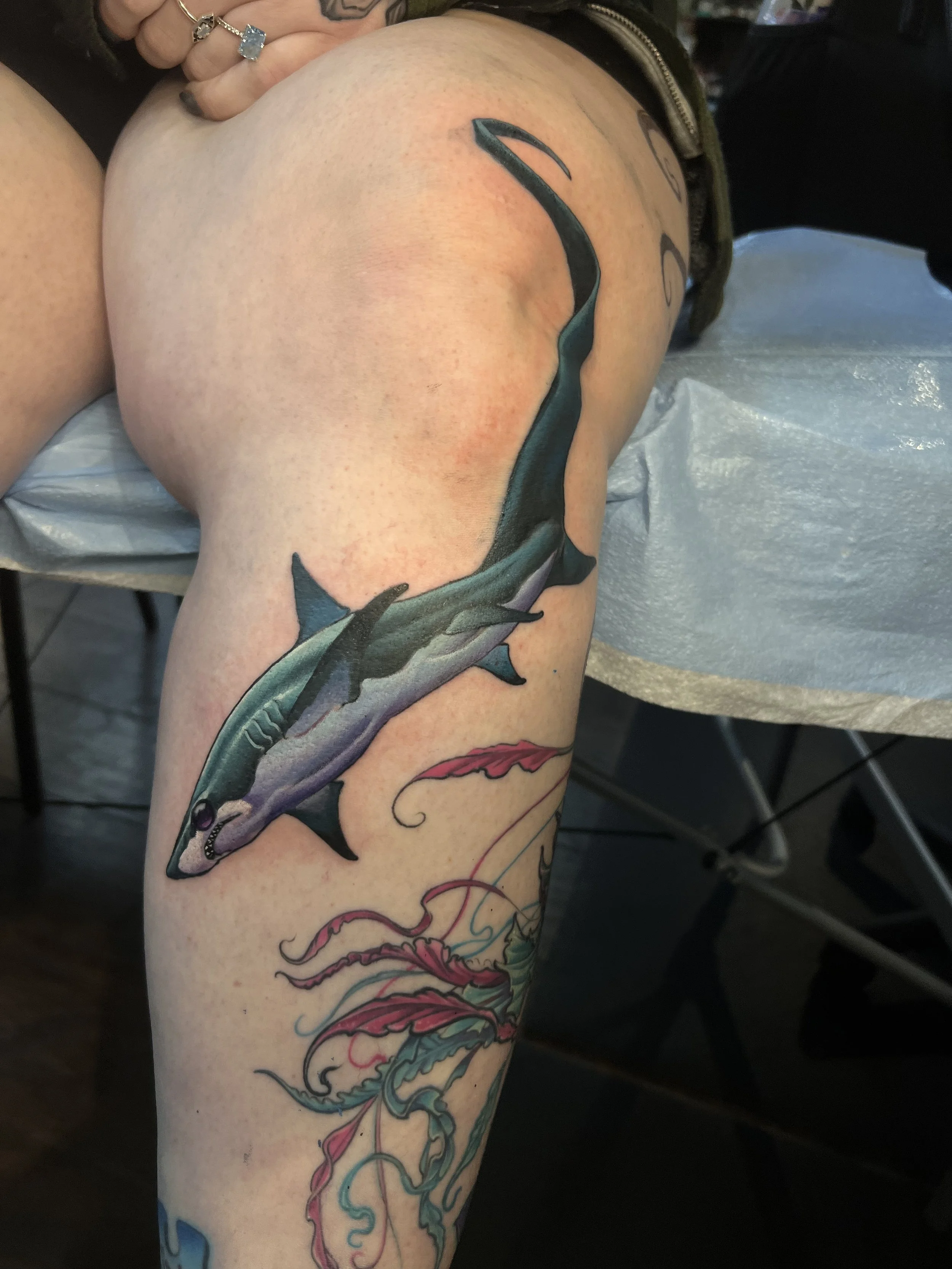 Colorful tattoo of a shark on a person's thigh.