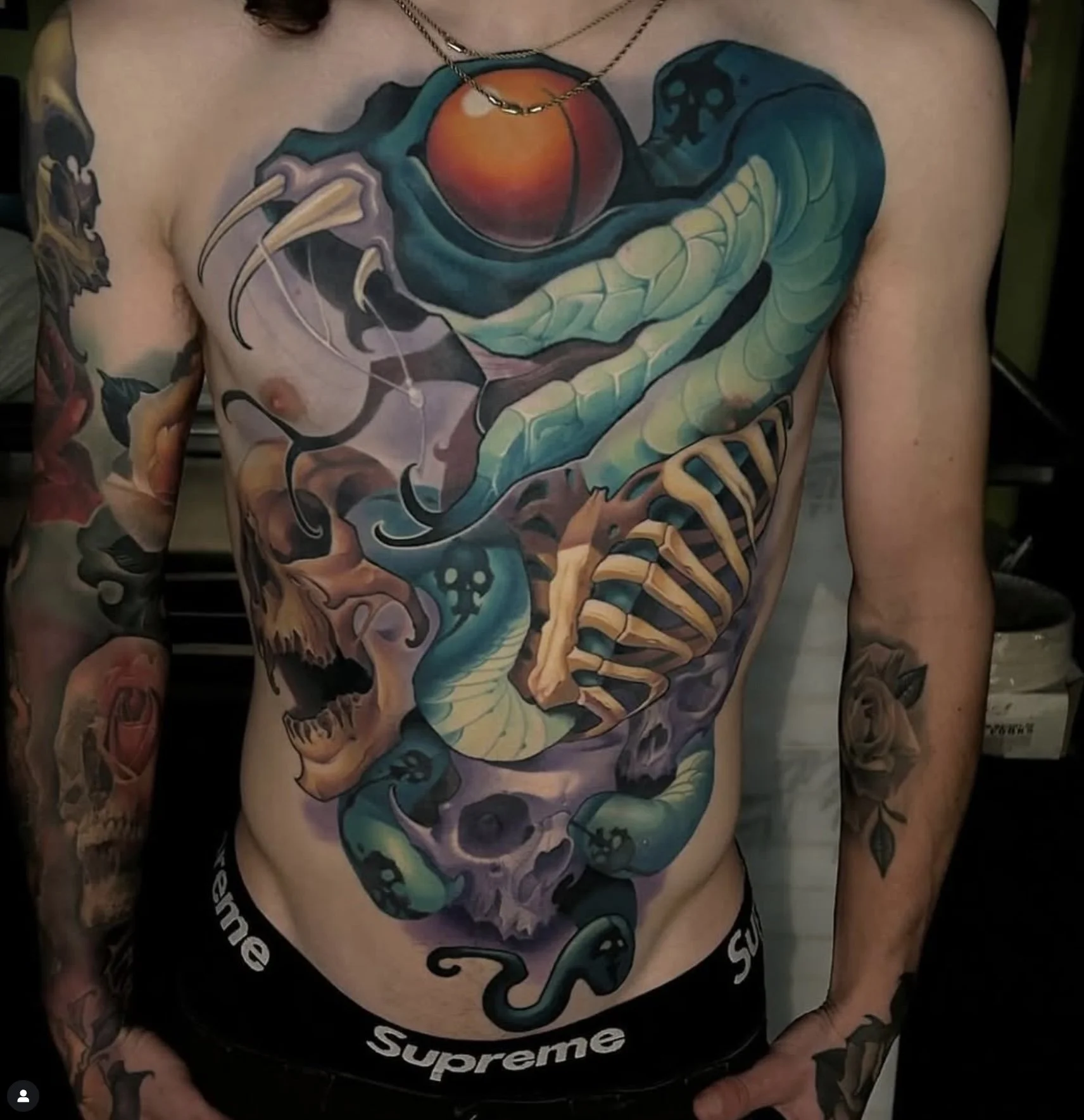 Colorful tattoo of a snake coiled around a skull on a man's chest, with additional tattoos on both arms.