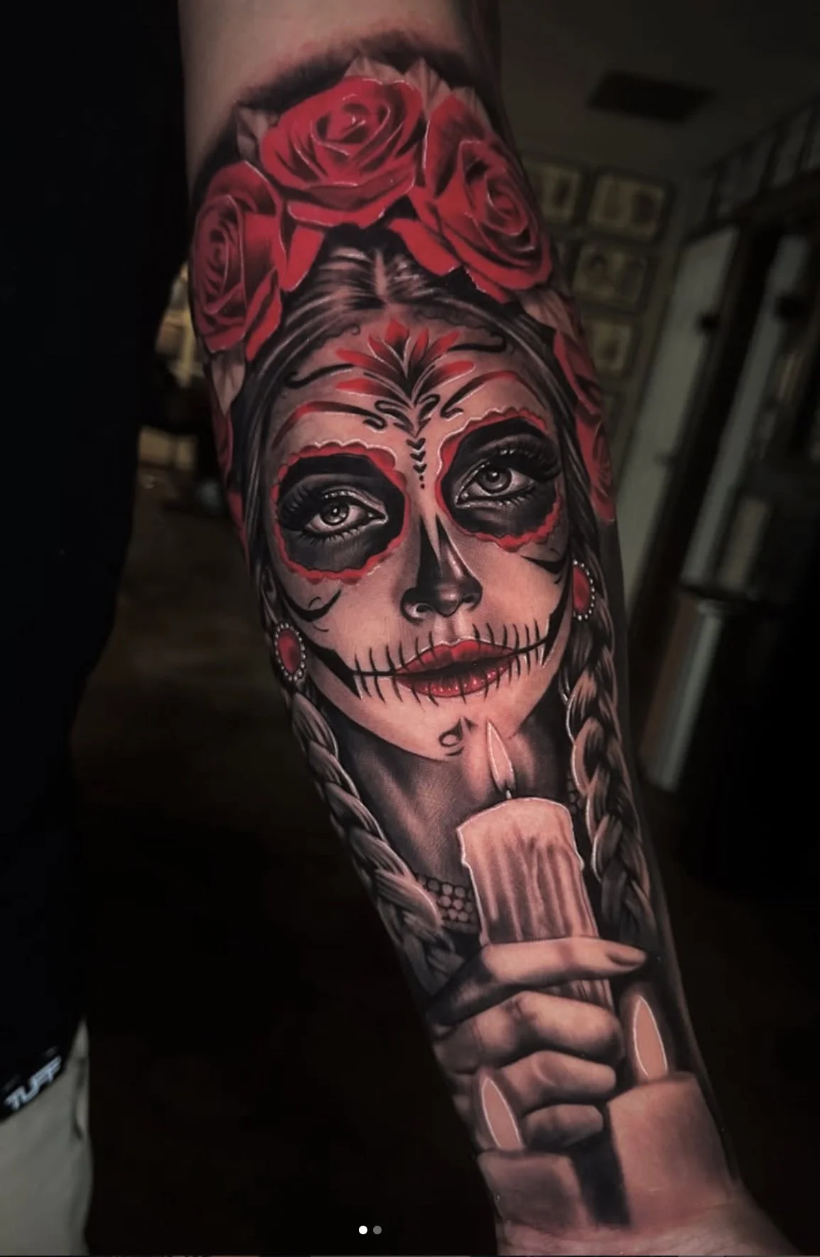 Tattoo of a woman with sugar skull makeup, roses on her head, holding a lit candle.