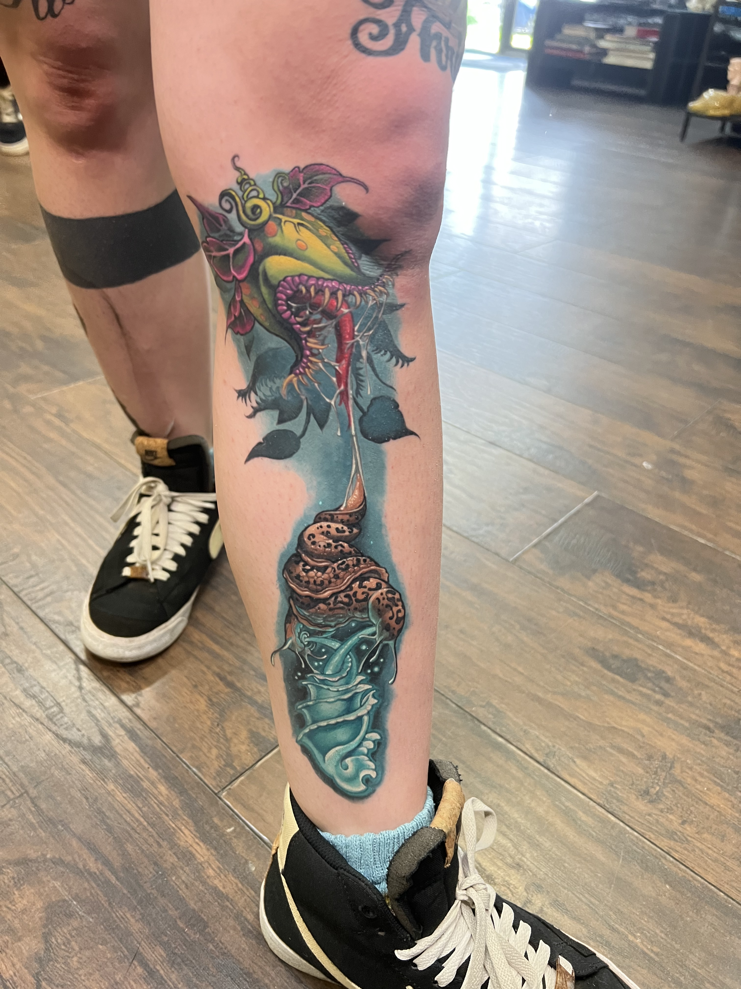 Colorful tattoo of a mythical creature on a person's leg, similar to a Venus fly trap.