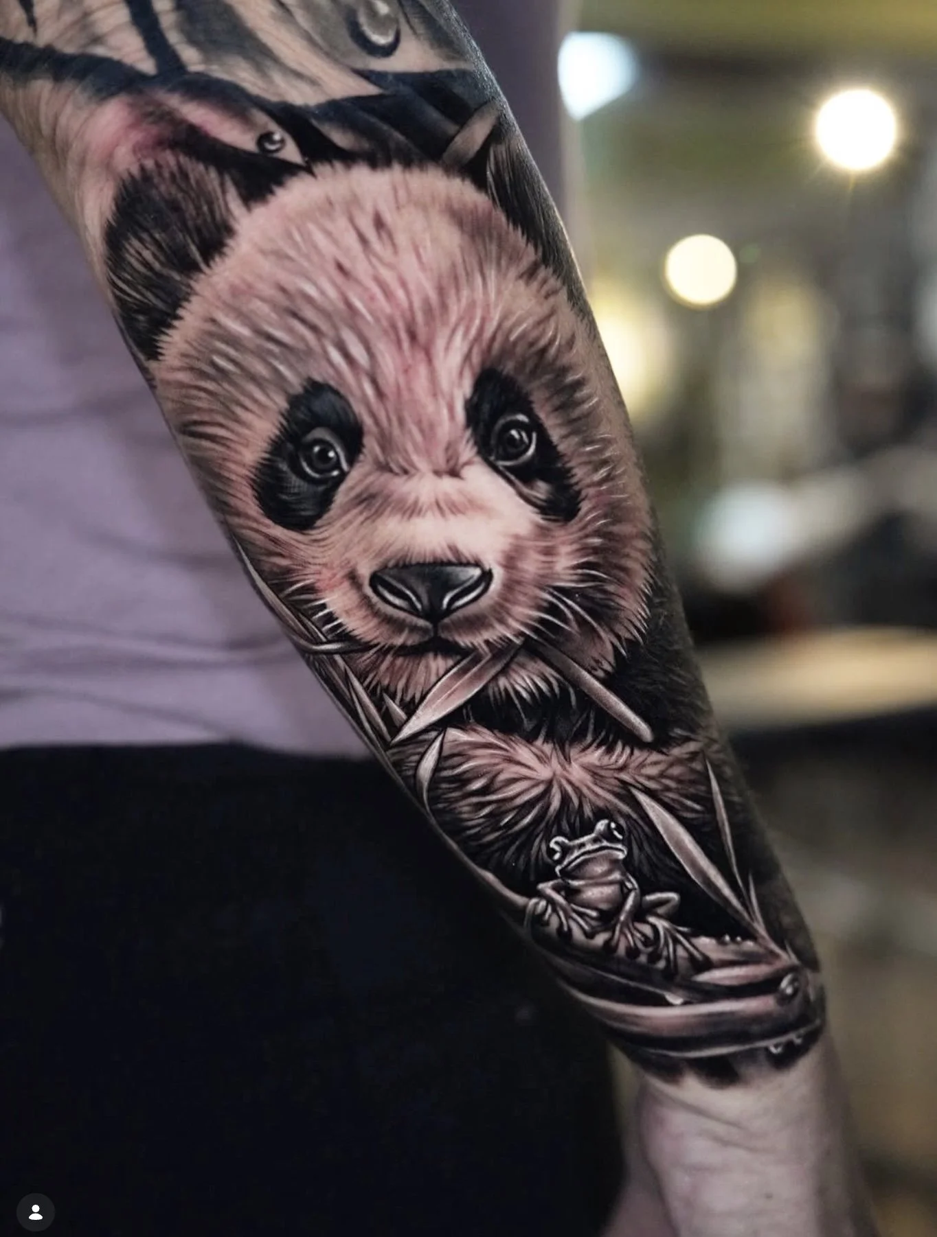 Tattoo of a baby sloth on a person's arm, with detailed fur and facial features, holding a small branch.