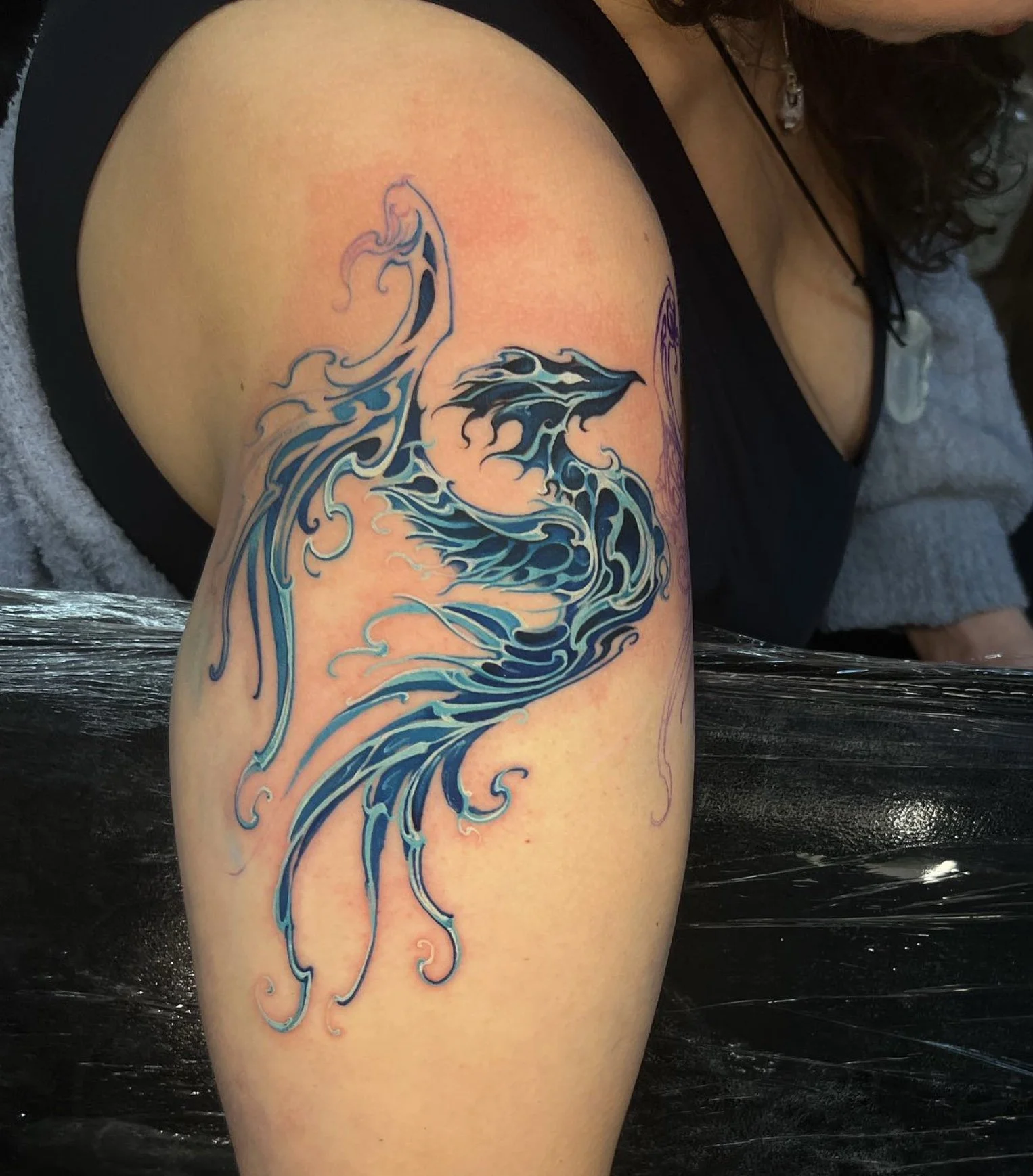 Colorful tattoo of a stylized blue and black dragon on person's upper arm.
