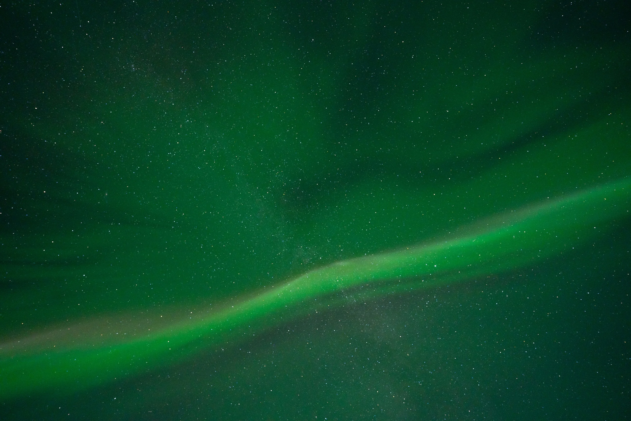 Green night sky with stars and a bright aurora borealis.