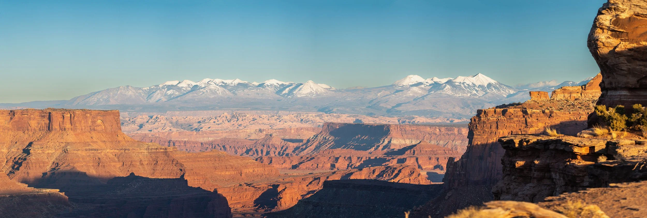 View of the Canyonlands National park with snow-capped mountains in the background, rocky cliffs in the foreground, and clear blue sky.