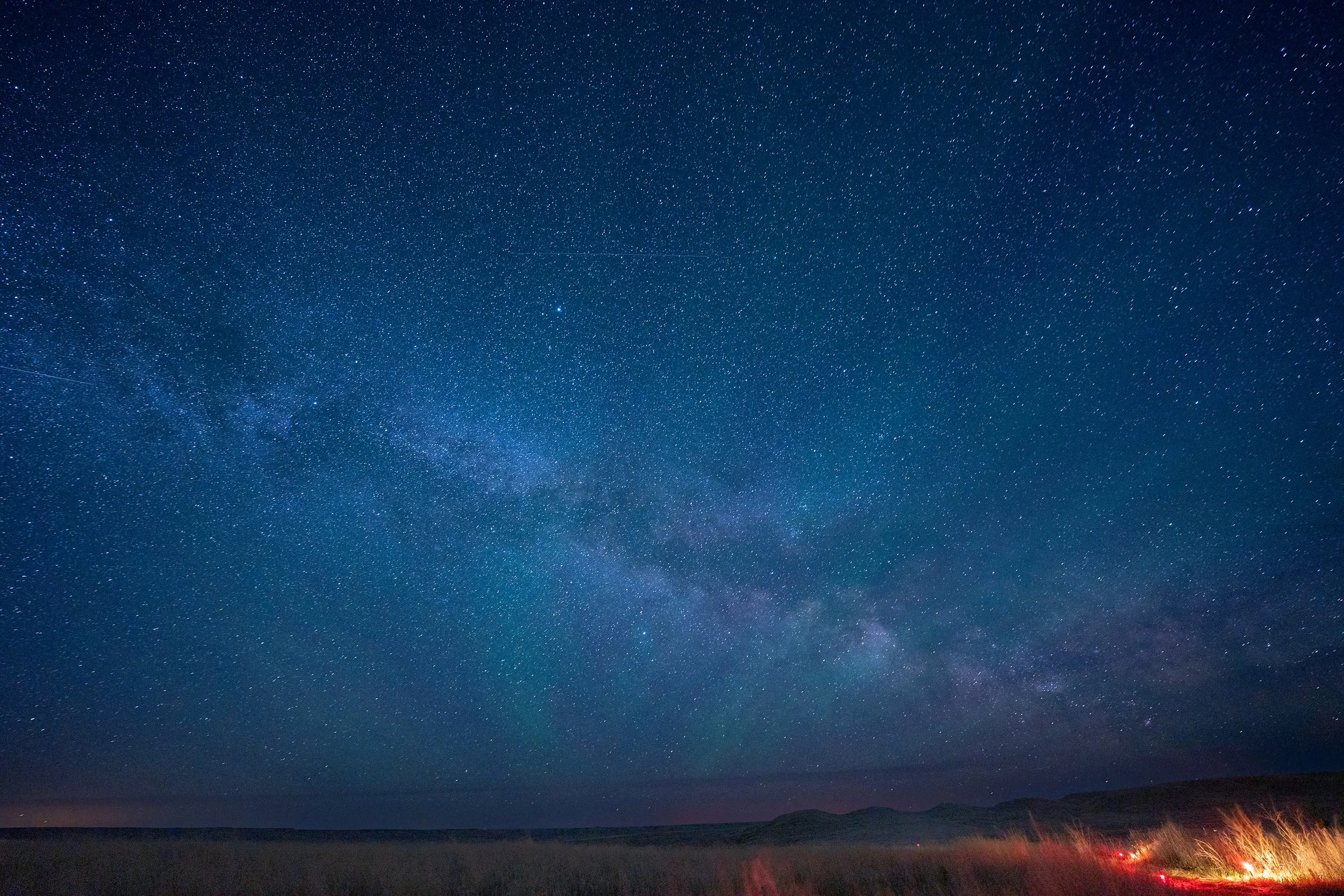 Night sky filled with stars over a landscape with mountains and a few distant lights.