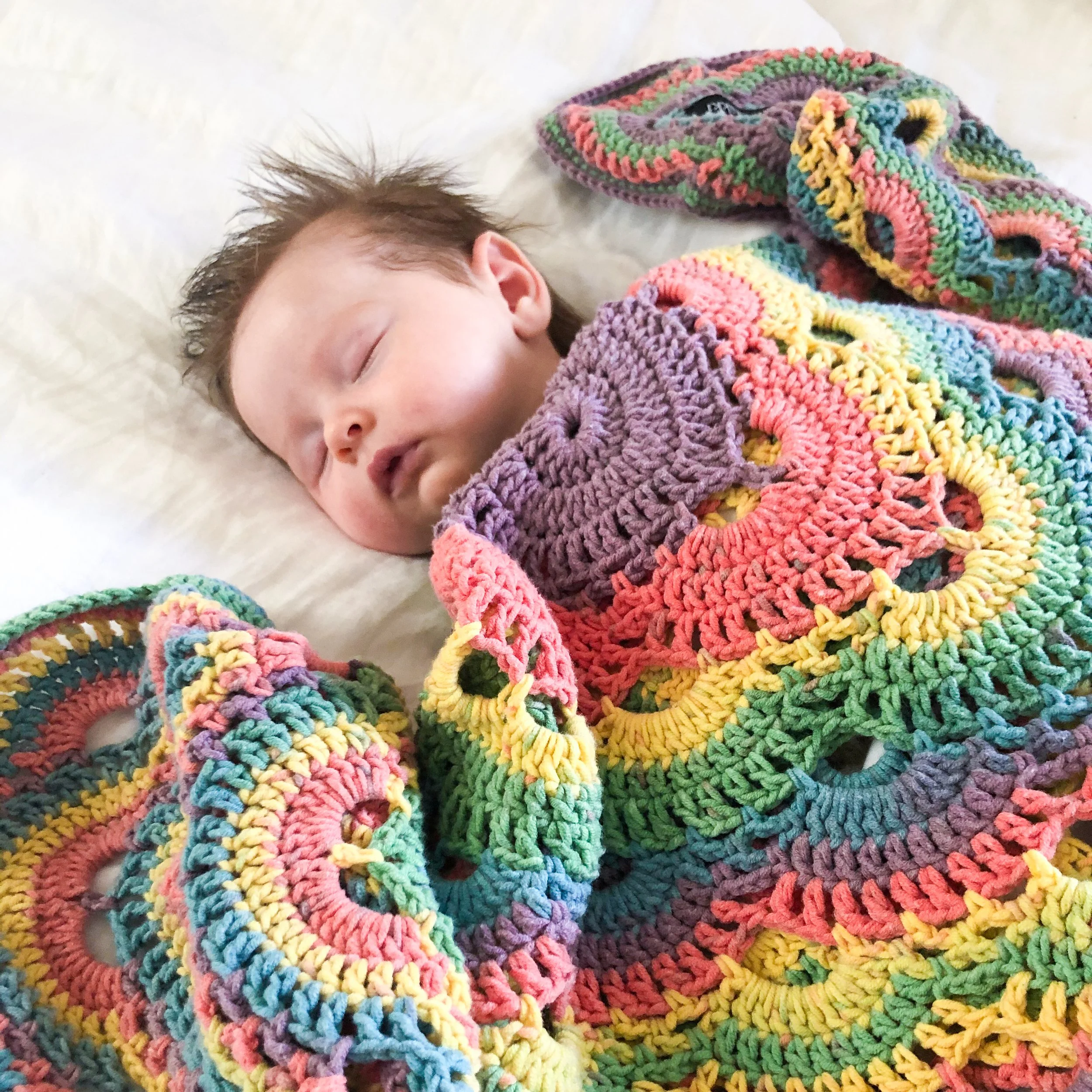 A beautiful baby is wrapped in a rainbow, custom made Pikki Nikki blanket