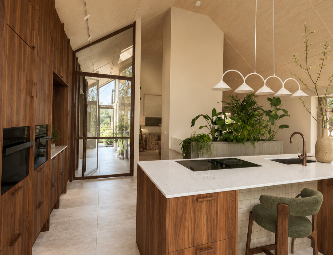 Modern kitchen with wooden cabinets, white countertops, green plants, and a view through glass doors to an outdoor area.