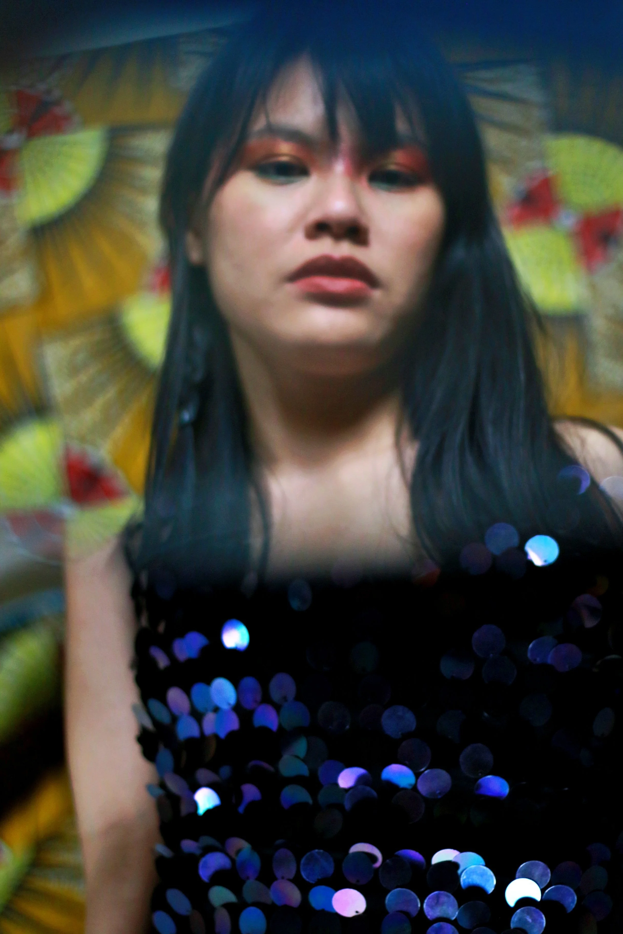 A striking portrait of a person with long dark hair and dramatic bronze eyeshadow directly forward with a confident, open expression. wears a black sequined garment, symbolising the personal power and radiant self-possession cultivated somatic sexual