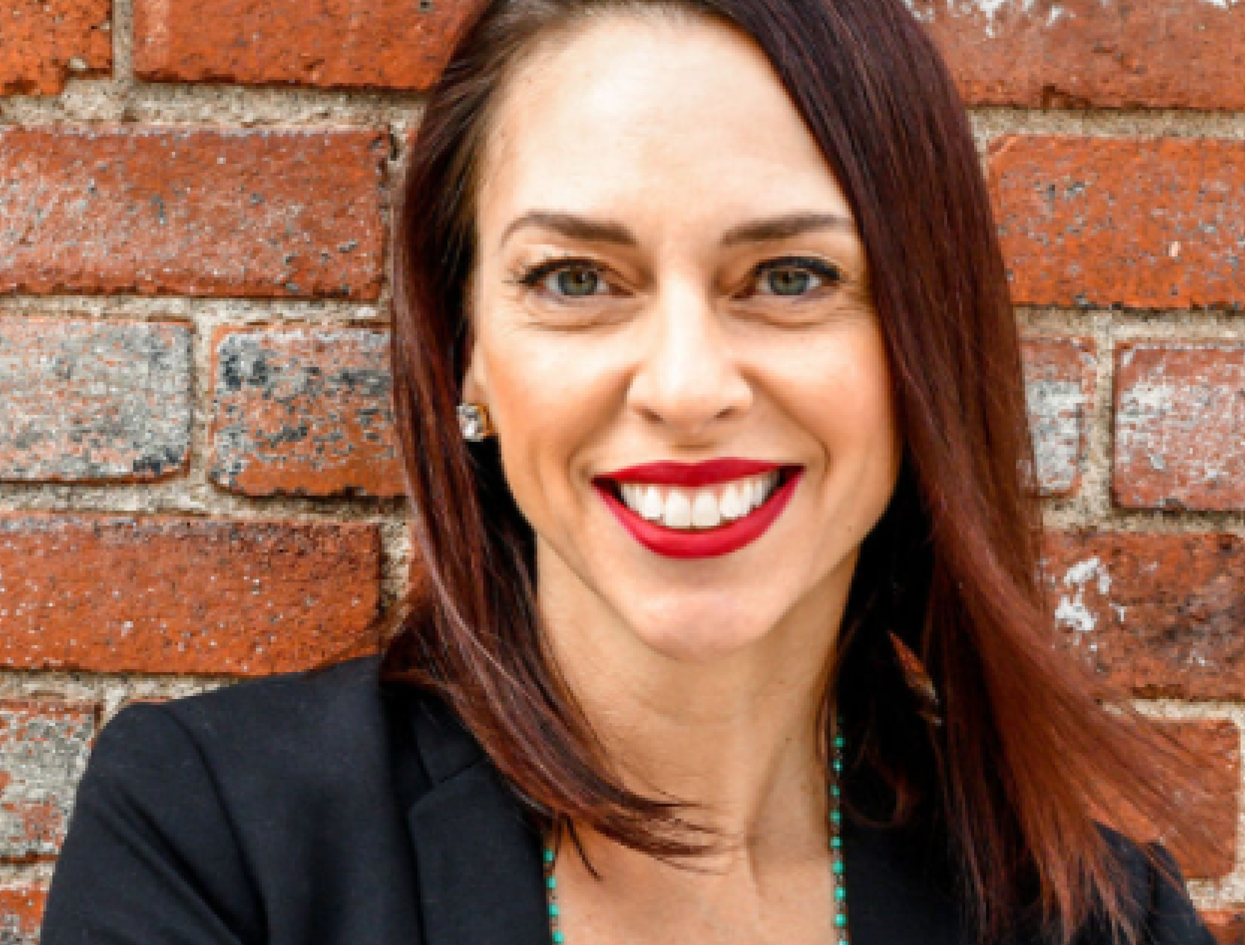 woman smiles in front of brick wall