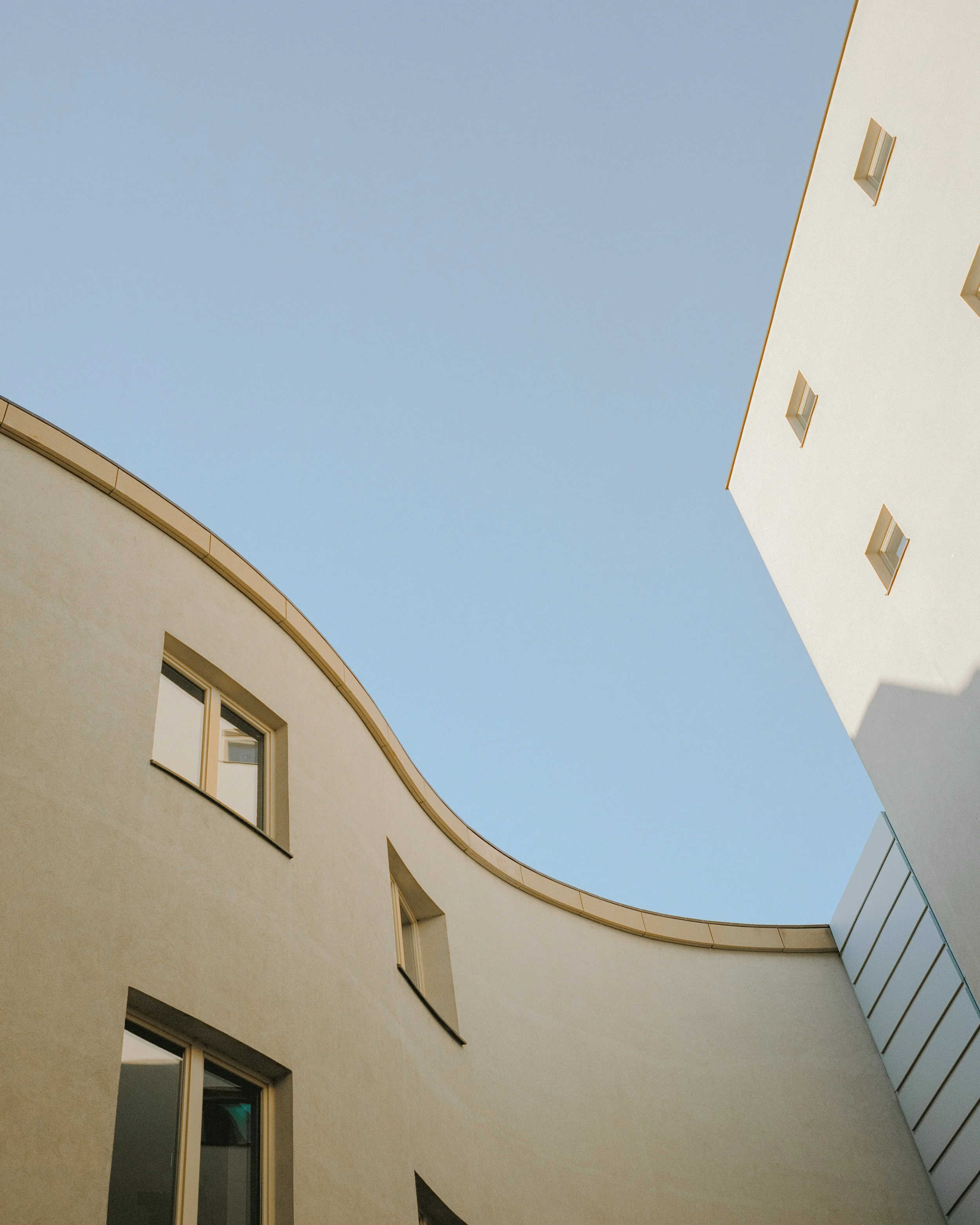 Moderne Architektur mit geschwungenen und geradlinigen Gebäudefassaden unter blauem Himmel.