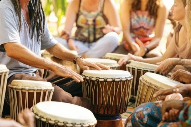 A group of people sitting in a circle playing drums together outdoors.