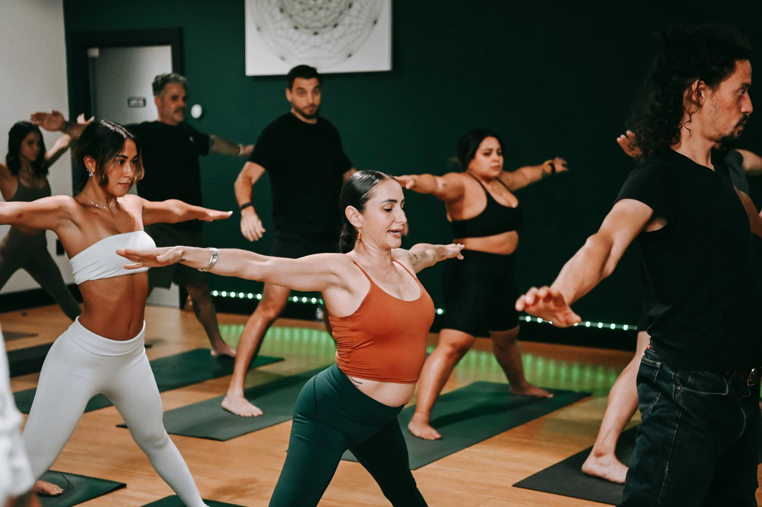 Group of diverse people practicing yoga in a studio, standing on yoga mats with arms extended outward.