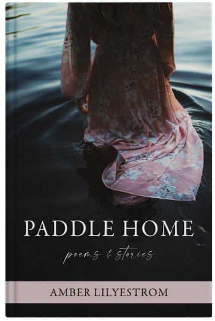 A woman in a pink floral dress kneeling in calm water at sunset, with a book titled "Paddle Home: Poems & Stories" by Amber Lilystrom in the foreground.