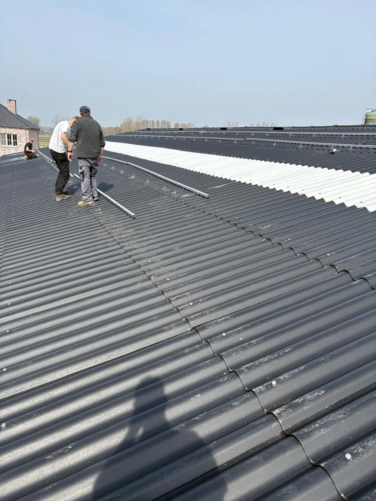 Voorbereiding zonnepaneleninstallatie op golfplaten dak met stokschroeven en montagerails.
