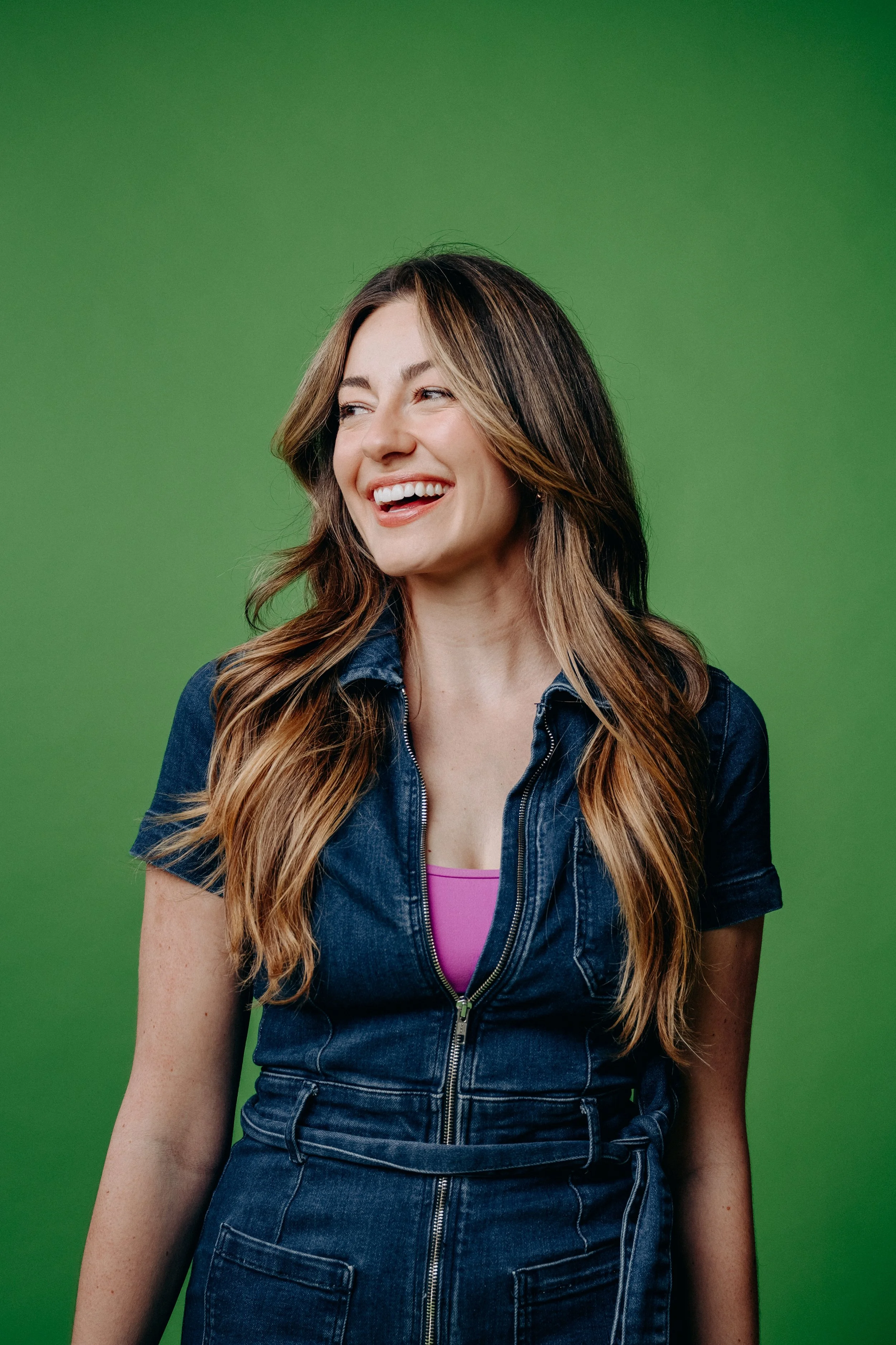 This is a picture of Marcelle, a Seattle-based hairstylist who works at Lady Neptune hair salon. She has long, bronde hair and is wearing a denim jumpsuit. She has a gigantic smile on her face which signals how warm and congenial she is all the time!