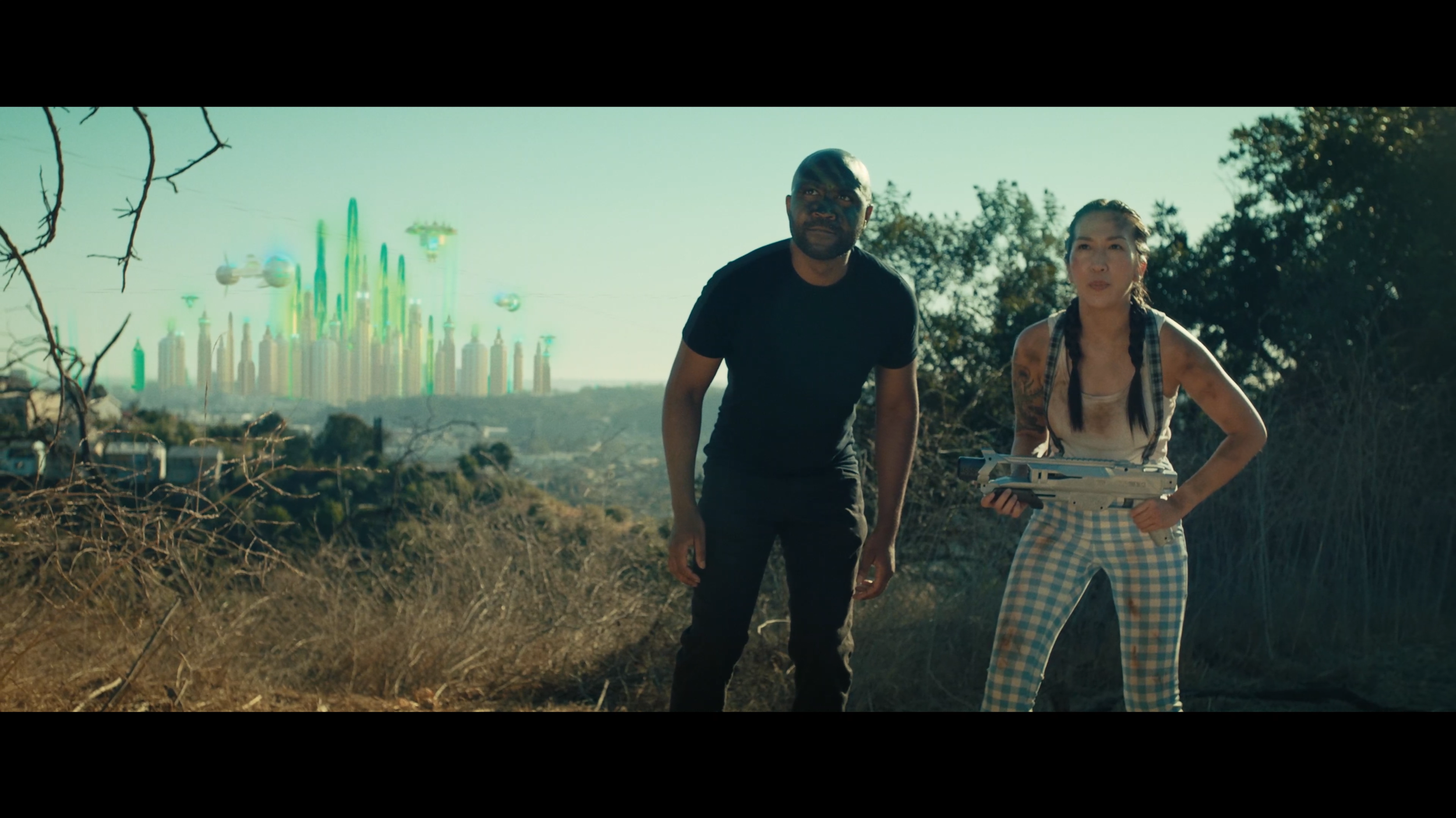 Actors Raphael Vargas Chestang and Kim Cooper stand next to a CGI version of the Emerald City of Oz.