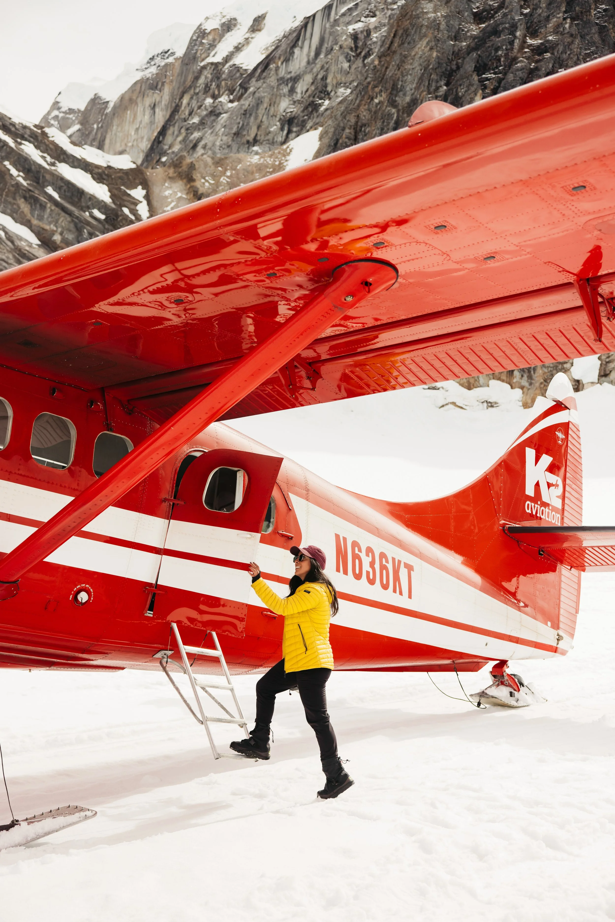 Woman stepping into a red ski plane on a glacier with rocky mountains behind during K2 Aviation glacier landing in Alaska