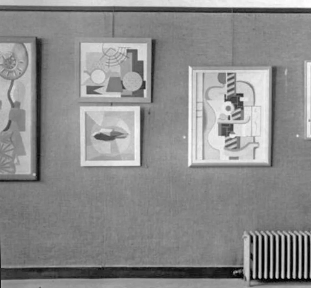 A plain wall displaying four abstract paintings in a gallery.