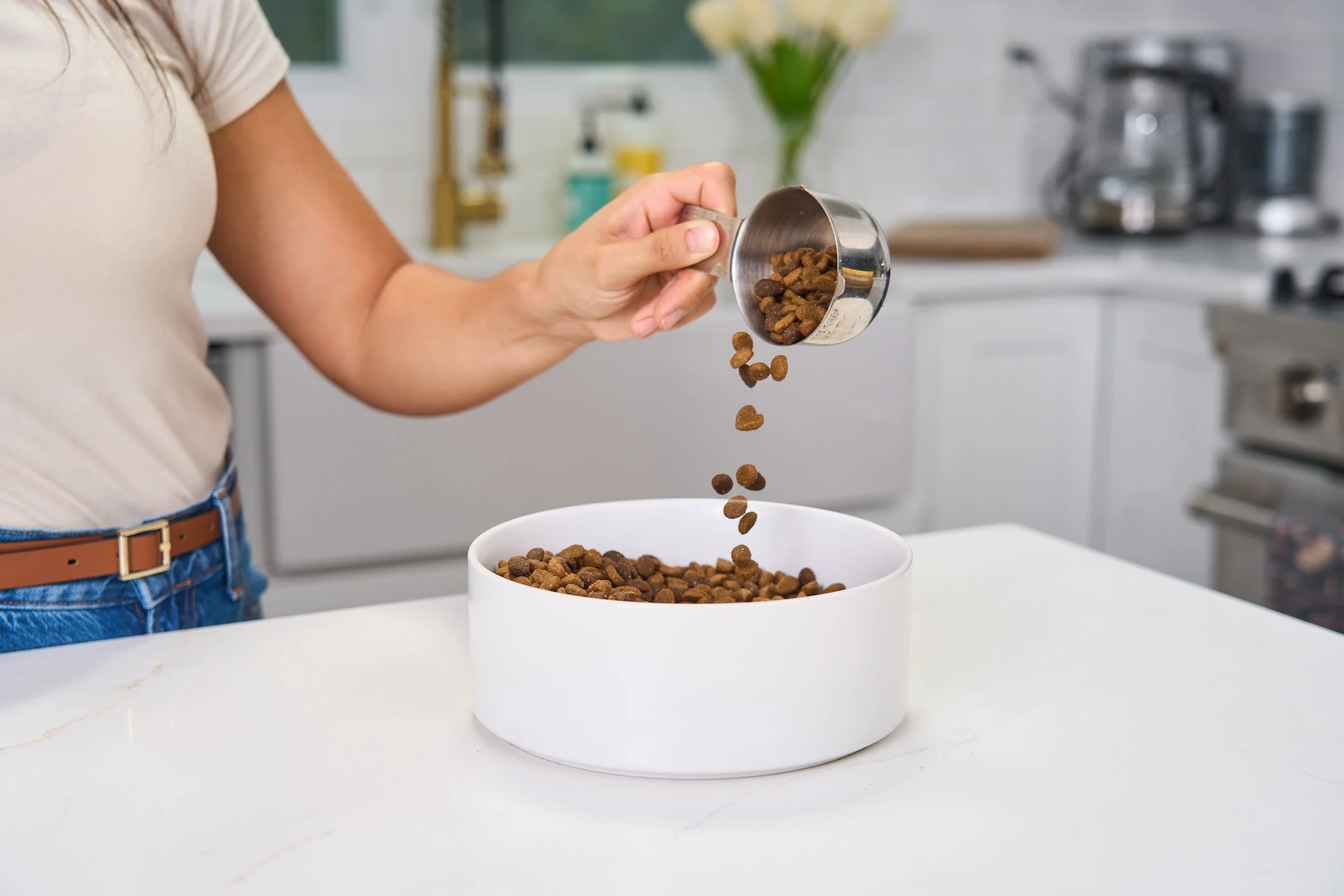 Lifestyle product photography image of a woman pouring dog food into a white bowl