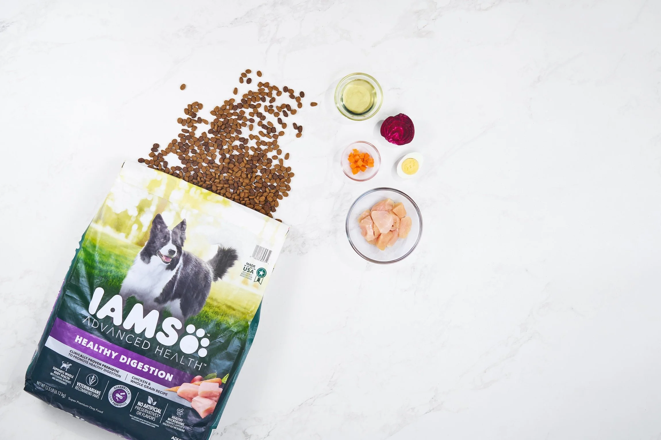 Flat Lay product photography of dog food bag with kibble and bowls with ingredients on a marble background