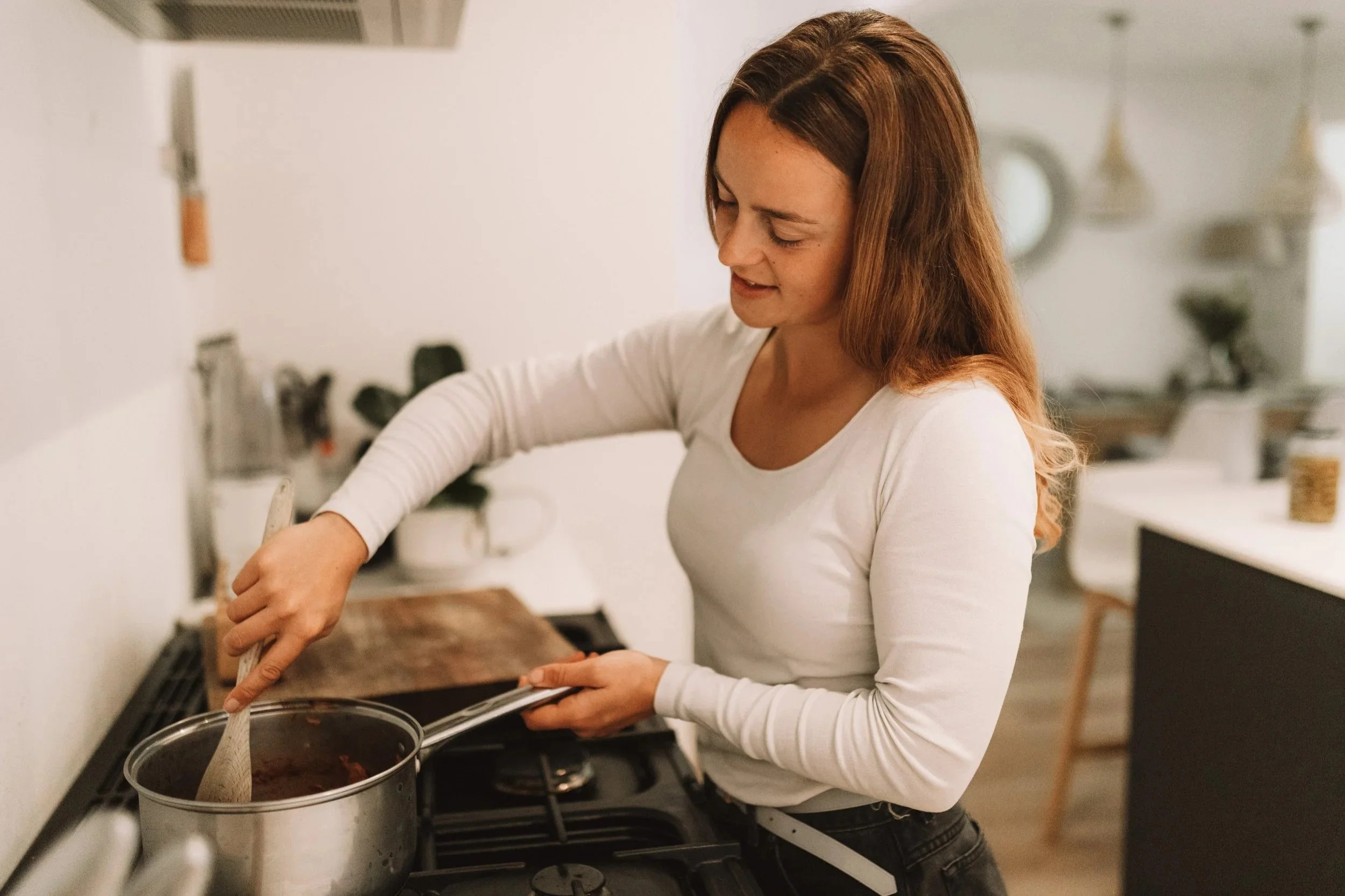 a woman standing in a bright kitchen, stirring a pot on the stove