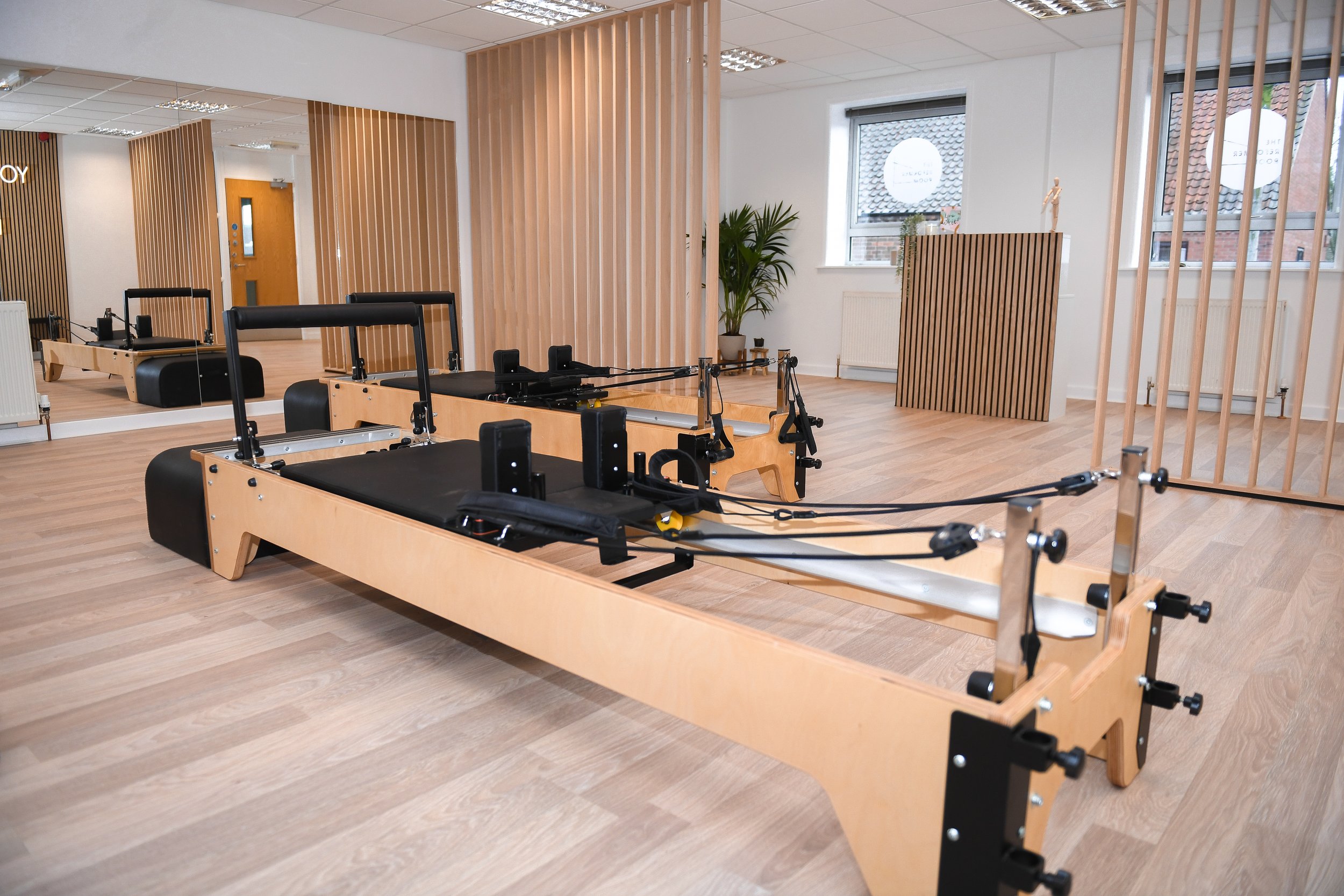 Pilates studio with reformer machines on wooden floor, large mirrors, and natural light.