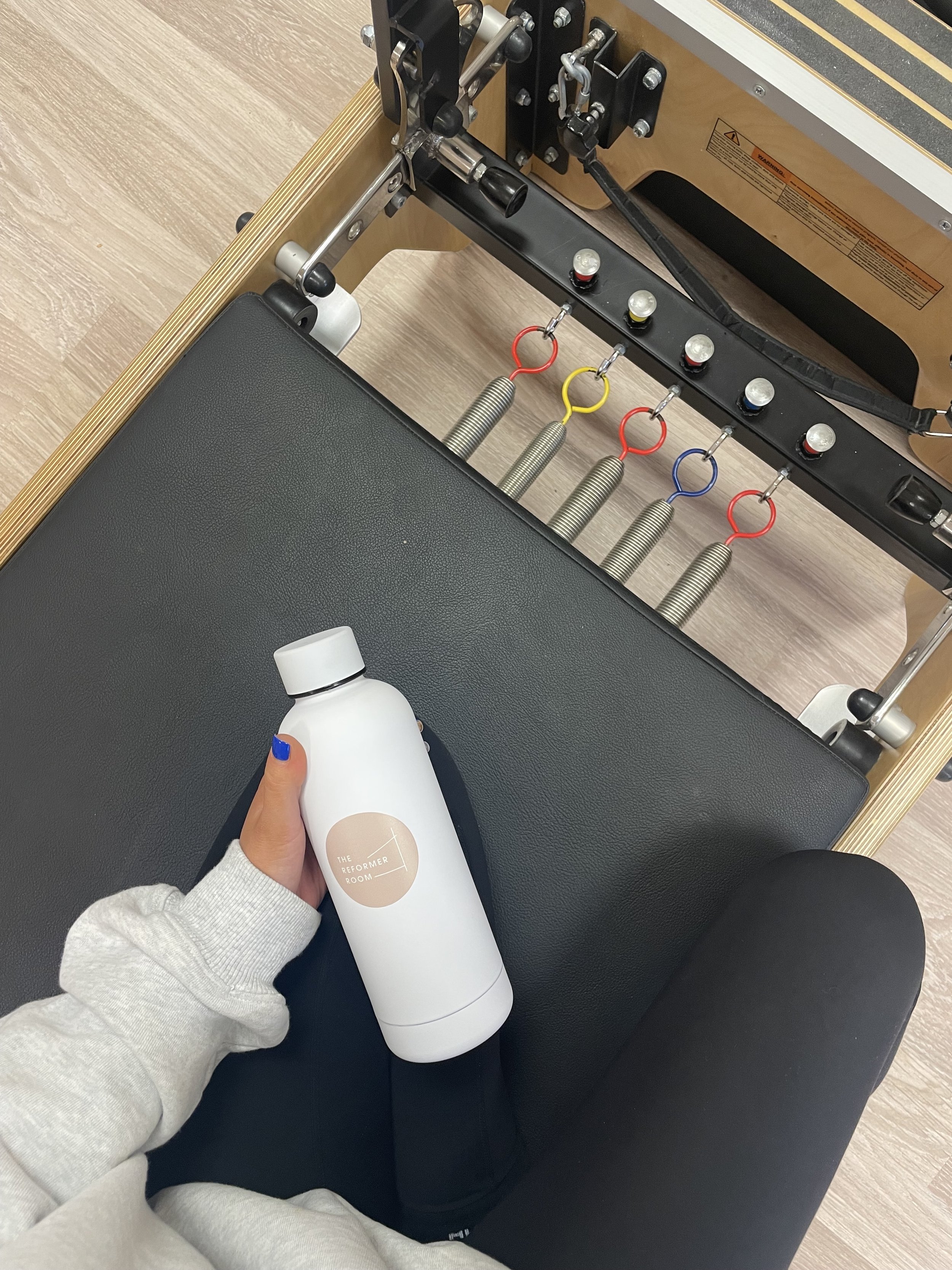 Person holding a white water bottle while sitting on a Pilates reformer machine.