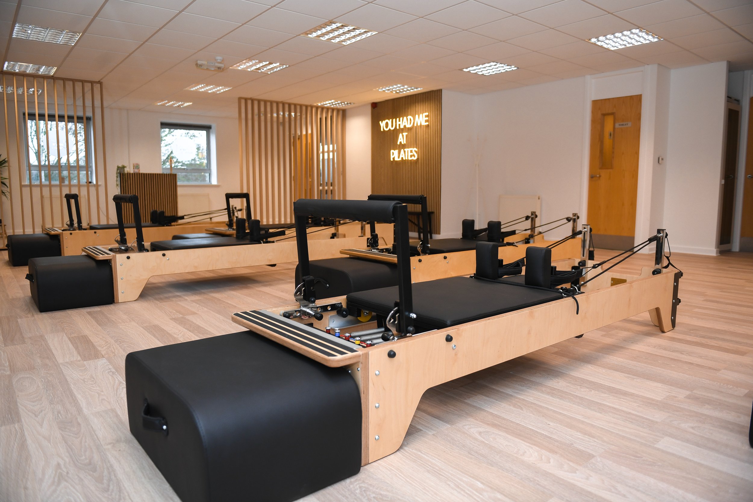 Pilates studio with reformer machines and "You Had Me at Pilates" sign.