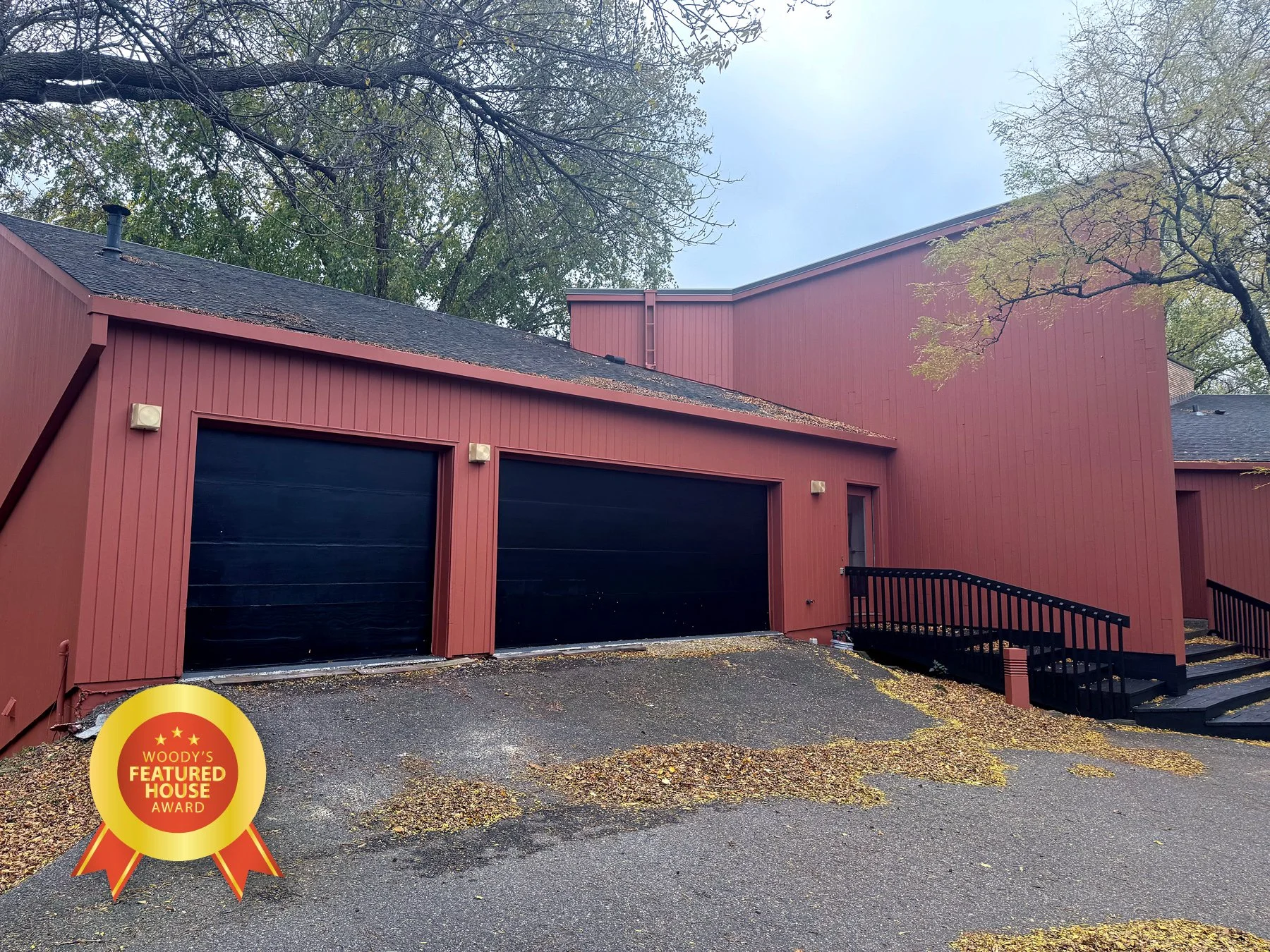 Red building with two black garage doors, stairs, and trees with falling leaves, Woody's Featured House Award badge in the lower left corner.