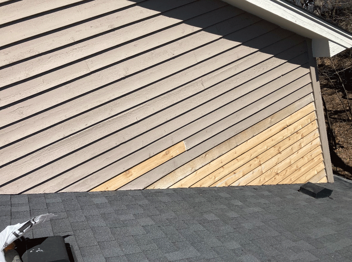 Photo of a house exterior showing a sloped wall with horizontal siding, partially covered with new wooden siding in the process of being installed. The roof with shingles is visible at the bottom of the image.