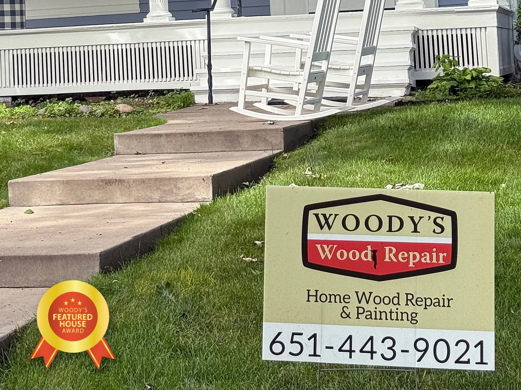 Sign for Woody's Wood Repair and Painting in front of a house with stairs and a rocking chair on the porch and a yard with grass.