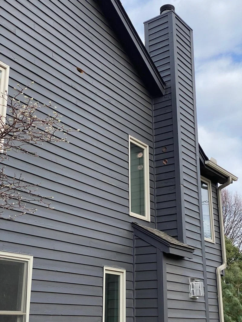A close-up of a blue house exterior with horizontal siding, multiple windows, and a chimney.