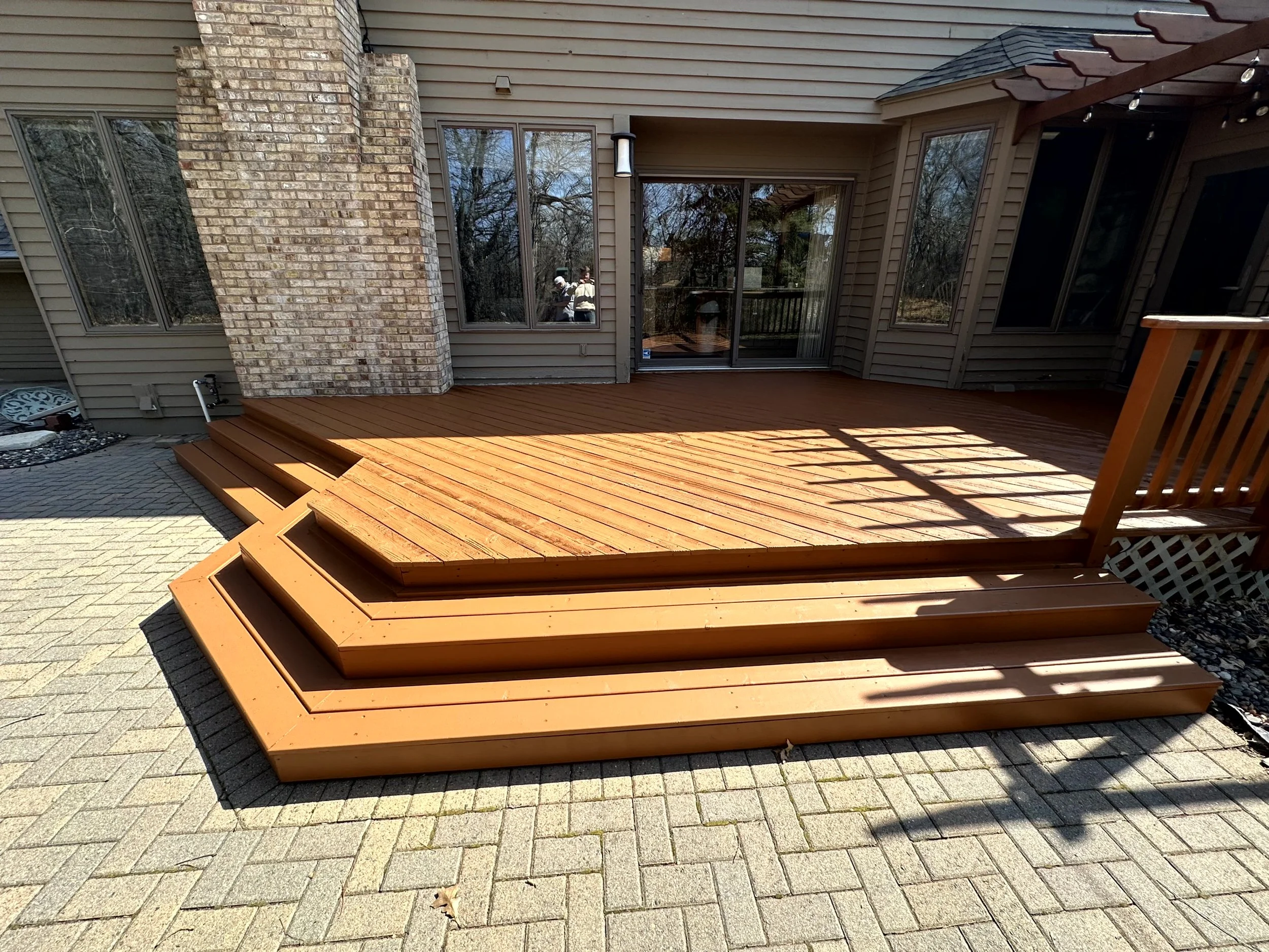 A newly built wooden deck attached to a house with large glass sliding doors, surrounded by a brick and siding exterior, with stairs leading up to the deck.