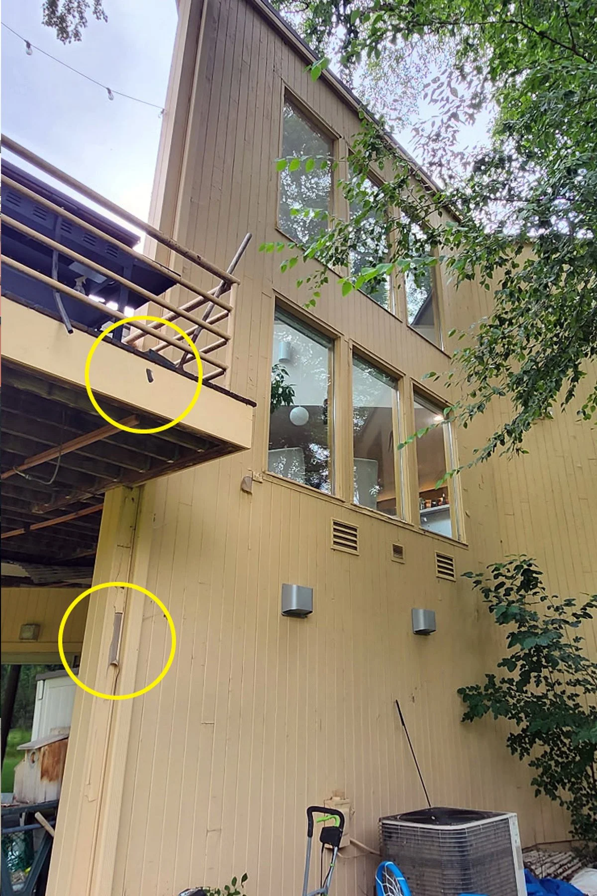 The exterior of a multi-story building with large windows, beige vertical siding, and two wall-mounted light fixtures. Two yellow circles damage on the building's wall that was later repaired.