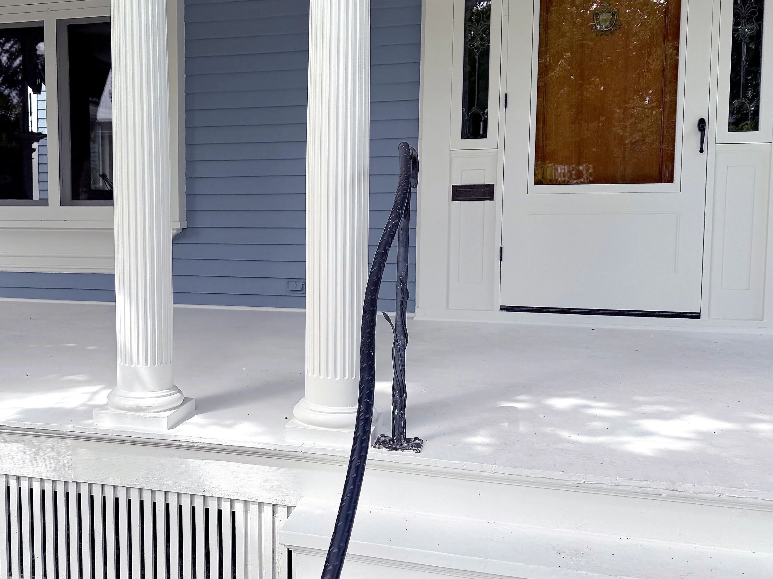 Front porch with white columns, a white railing, a blue house wall, and a white door with a window.