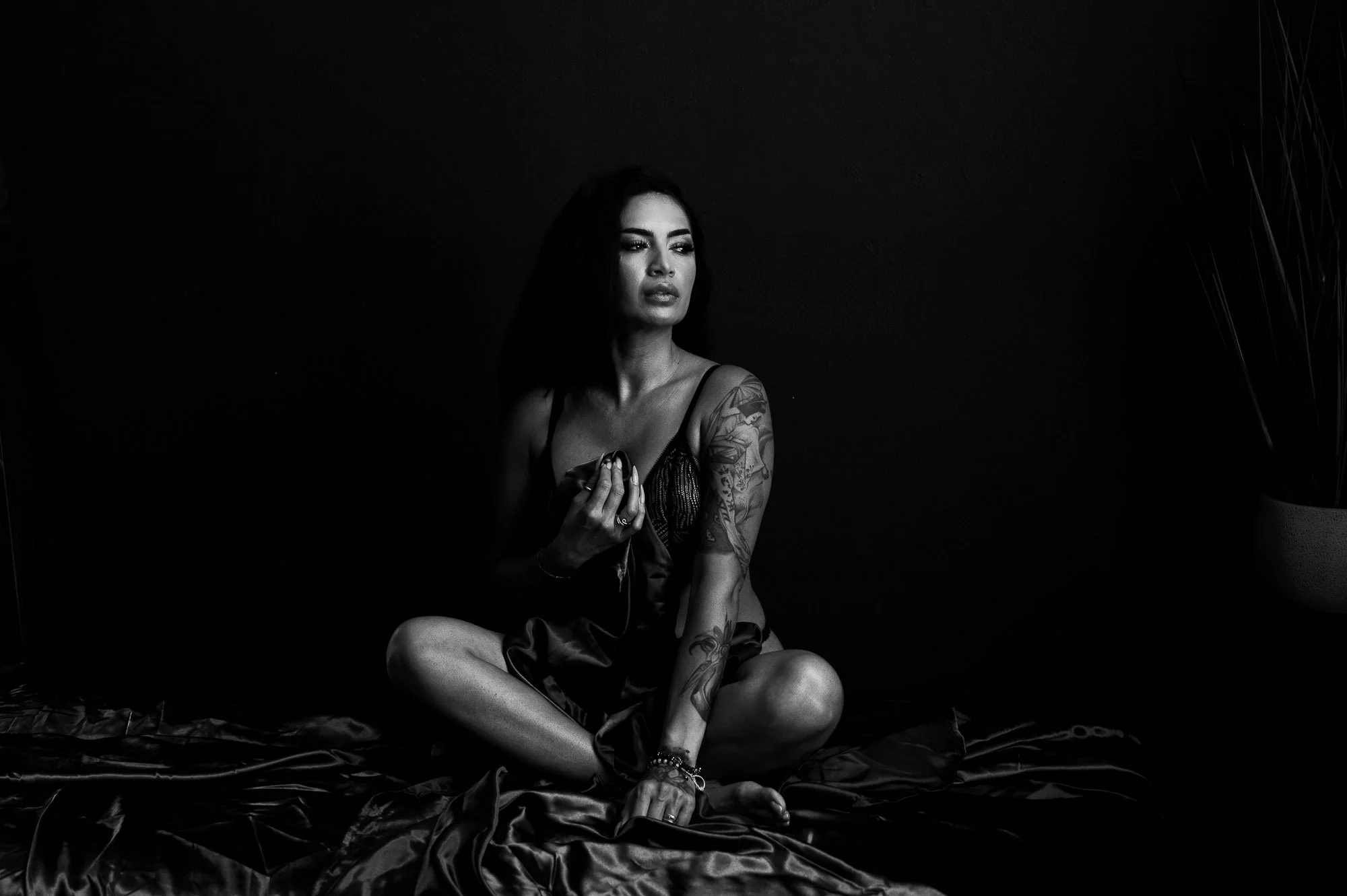 Black and white boudoir portrait of a woman sitting cross legged on a bed at Black Kat Studios in Los Angeles