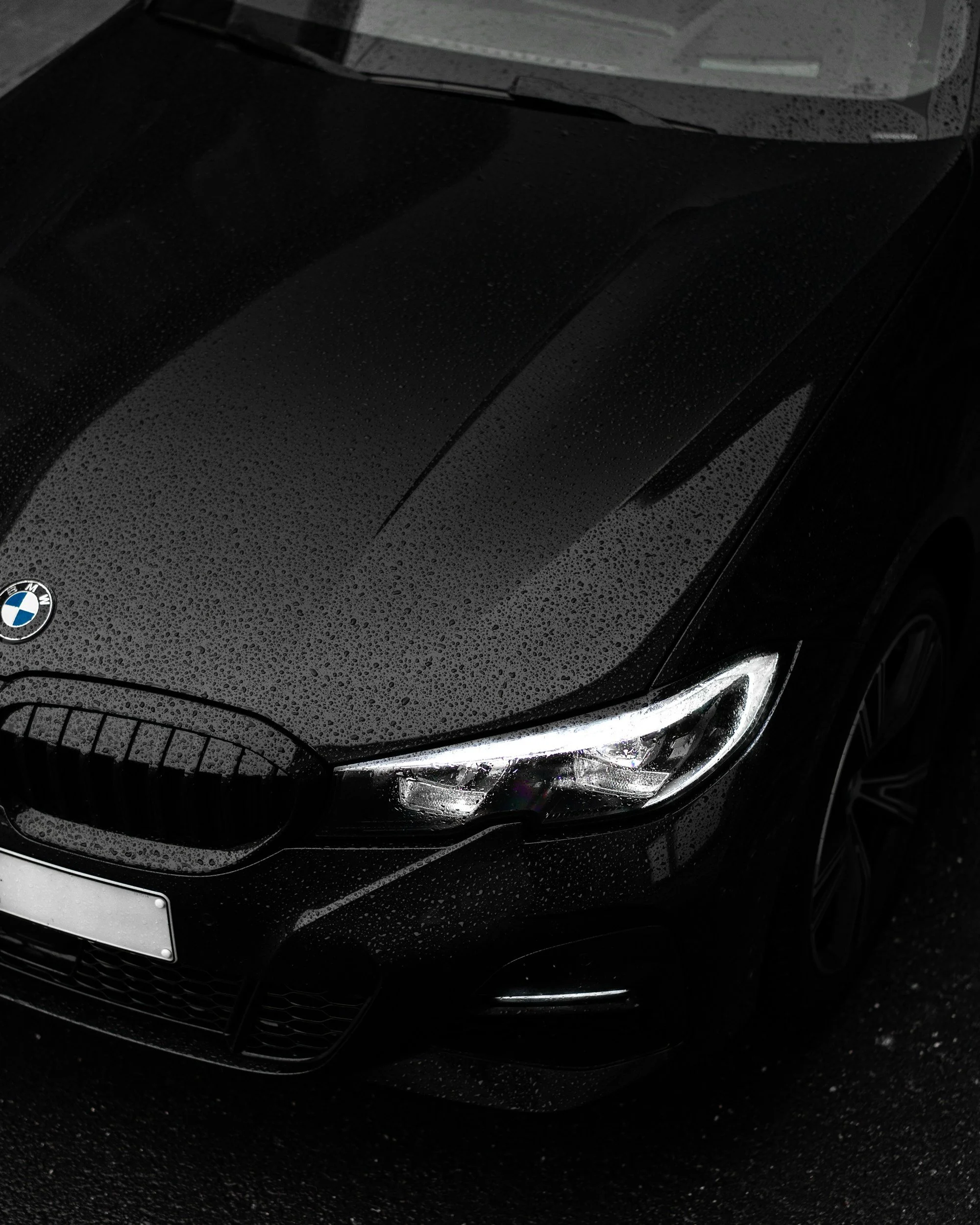Glossy black luxury vehicle with water beading across the hood.