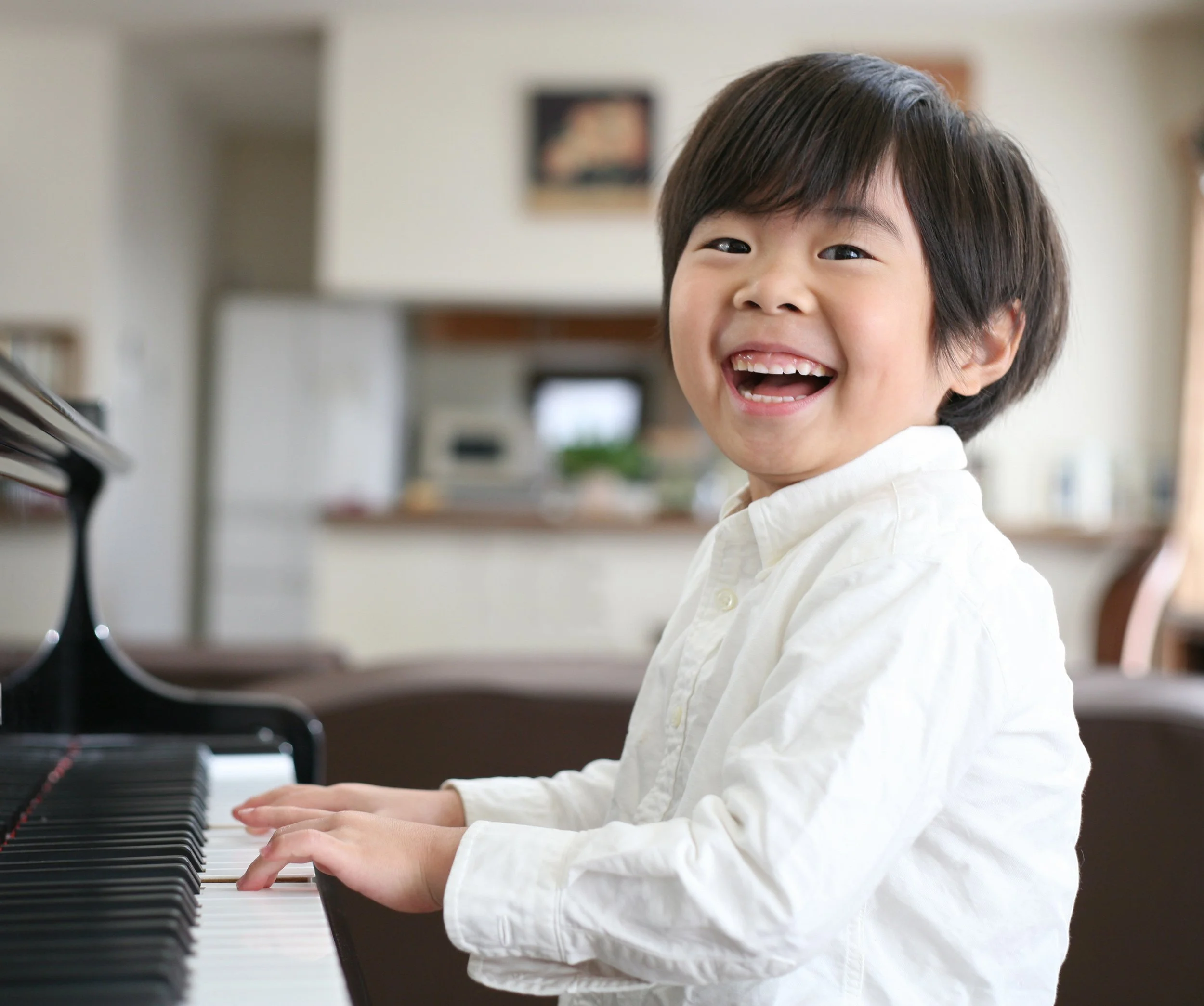 A young boy sat at the piano, playing and smiling happily.