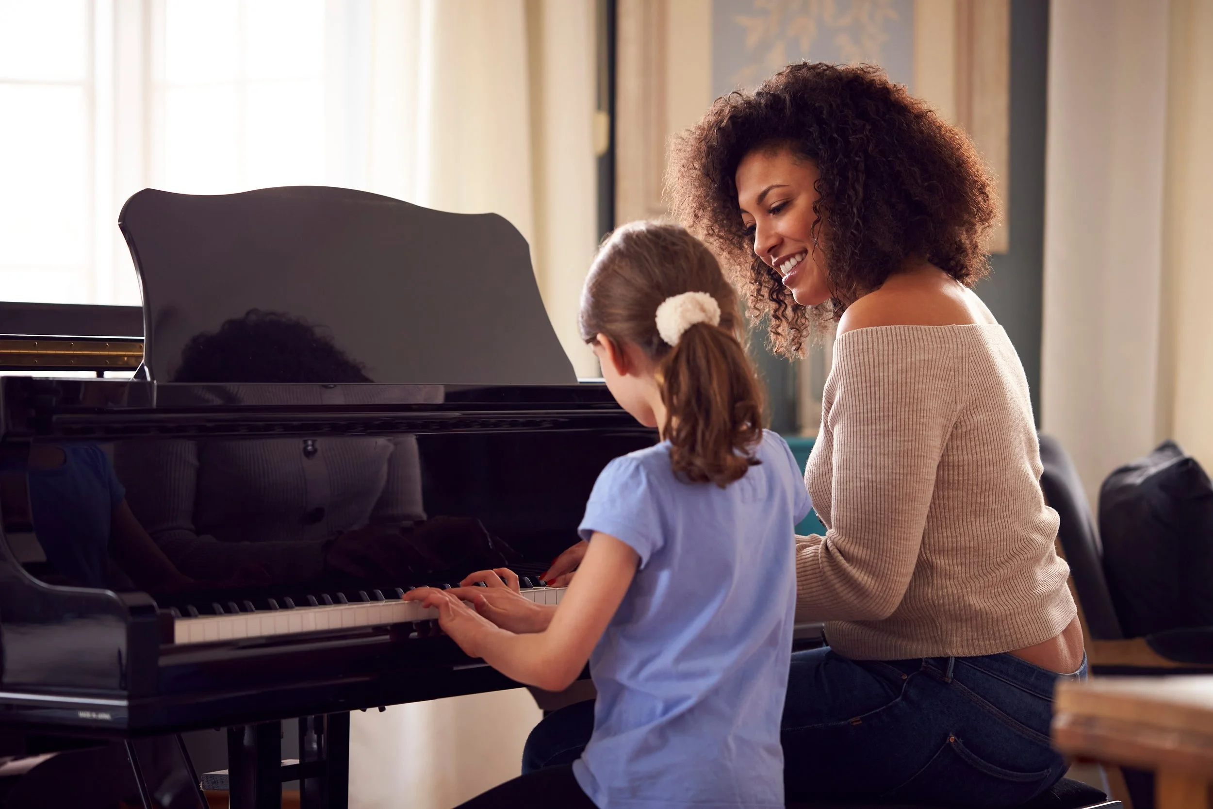 A woman with curly hair is helping a young girl learn to play the piano.