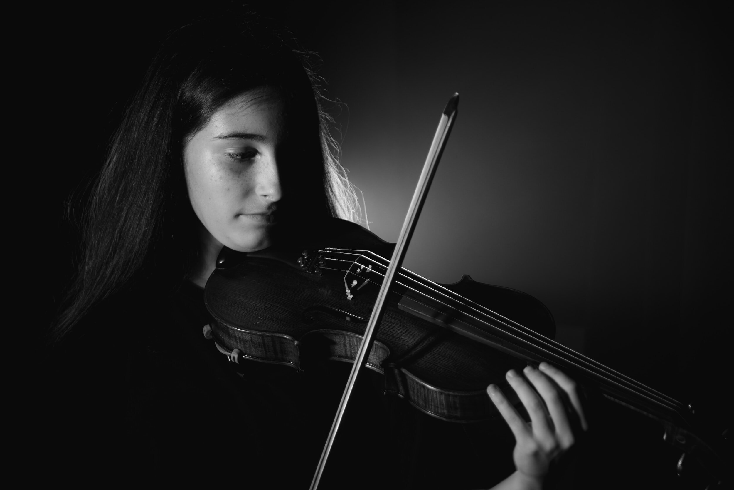 A teenage girl playing the violin with a bow.
